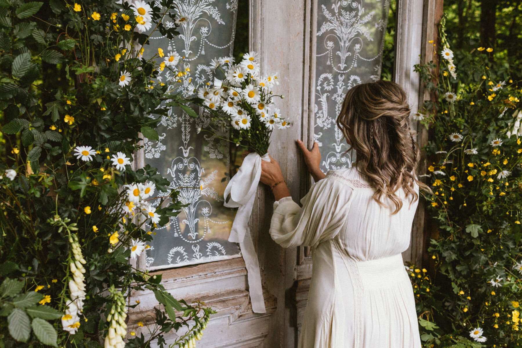 Wickerwood Farm, an Eco Friendly, Glamping Wedding Venue in East Sussex 8 Bride holding a bouquet of daisies opening an antique door frame. Wedding props at Wickerwood Farm wedding venue, East Sussex.