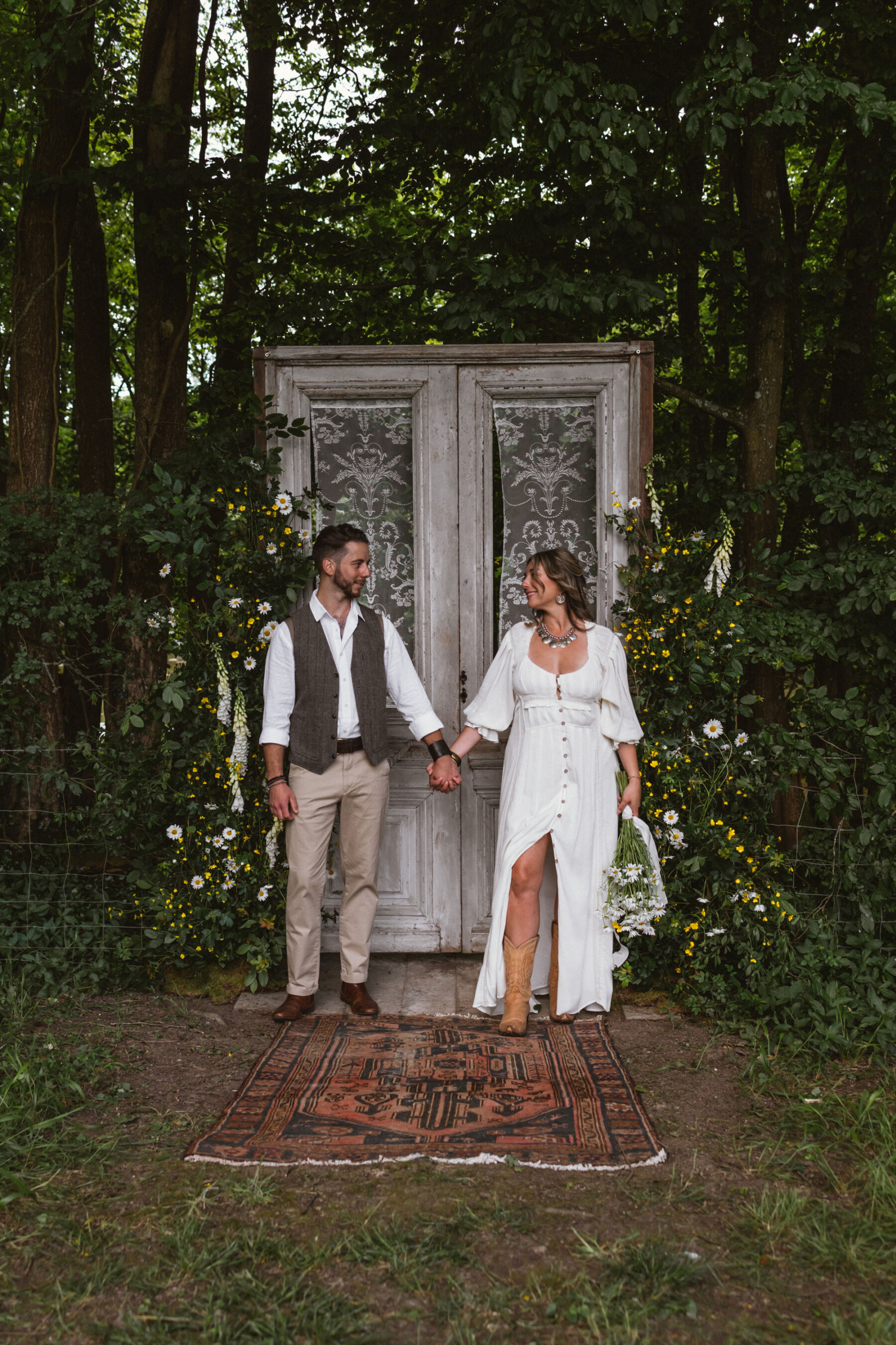 Wickerwood Farm, an Eco Friendly, Glamping Wedding Venue in East Sussex 12 Bride and groom standing in front of a large antique wooden doorframe that has been positioned inside the woodland at Wickerwood Farm wedding venue, East Sussex.