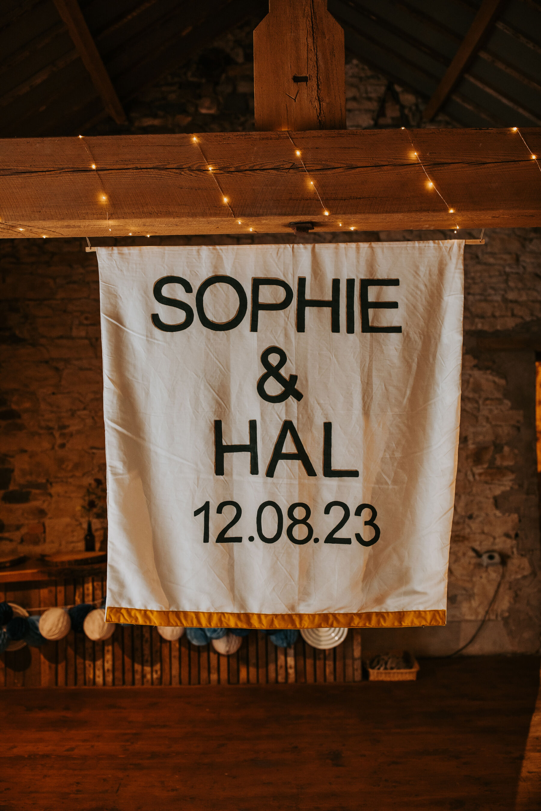Sophie & Hal's Joyful, Colourful & Sustainable DIY Barn Wedding at Low Hall The Lakes 45 Wedding banner of the couple's names and the date of their wedding hanging inside the wedding barn at Low Hall The Lakes.