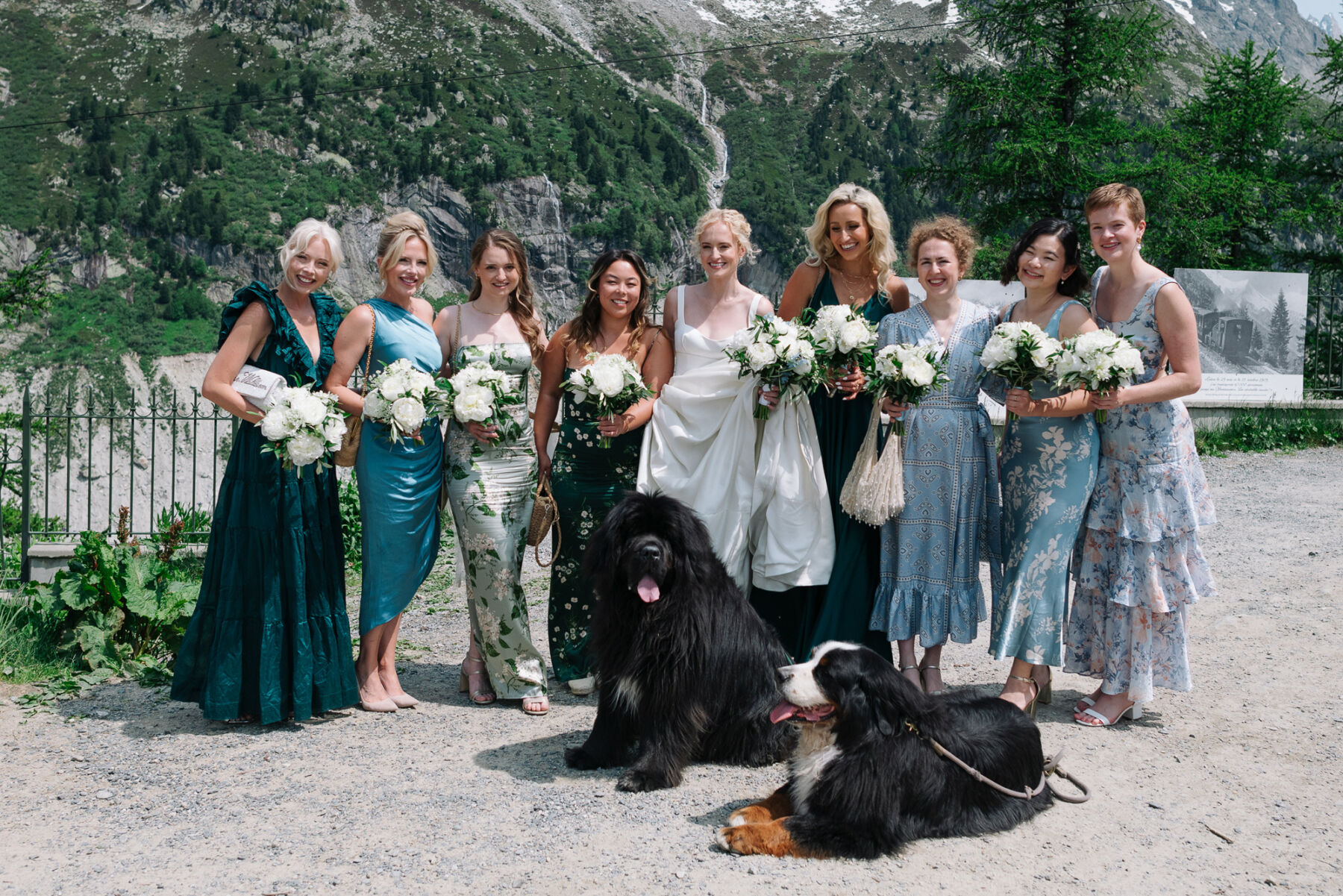 Georgia in Emilia Wickstead, For Her Classy & Elegant Black Tie Mountain Wedding in the Chamonix 17 Chamonix wedding, with bridesmaids in mismatched blue dresses. The bridal party each carry white bouquets and close by, two huge black dogs sit on the floor.
