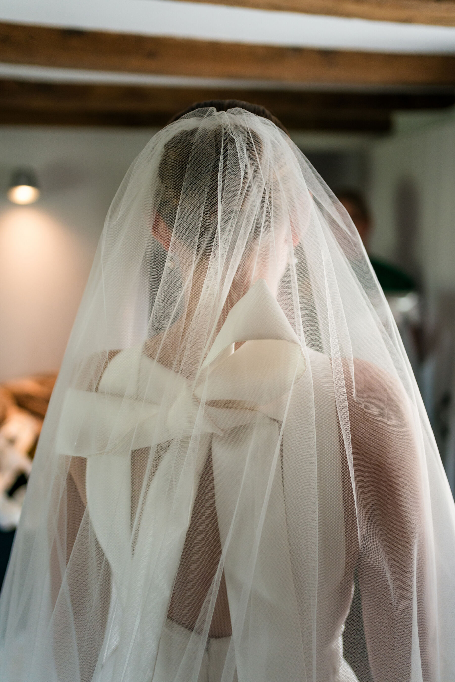Alice Wore Oak by Halfpenny London For Her Charming Spring Marquee Wedding in Suffolk 17 Bride getting ready in her Oak by Halfpenny London wedding dress with a large bow at the back and a blusher veil over her face.