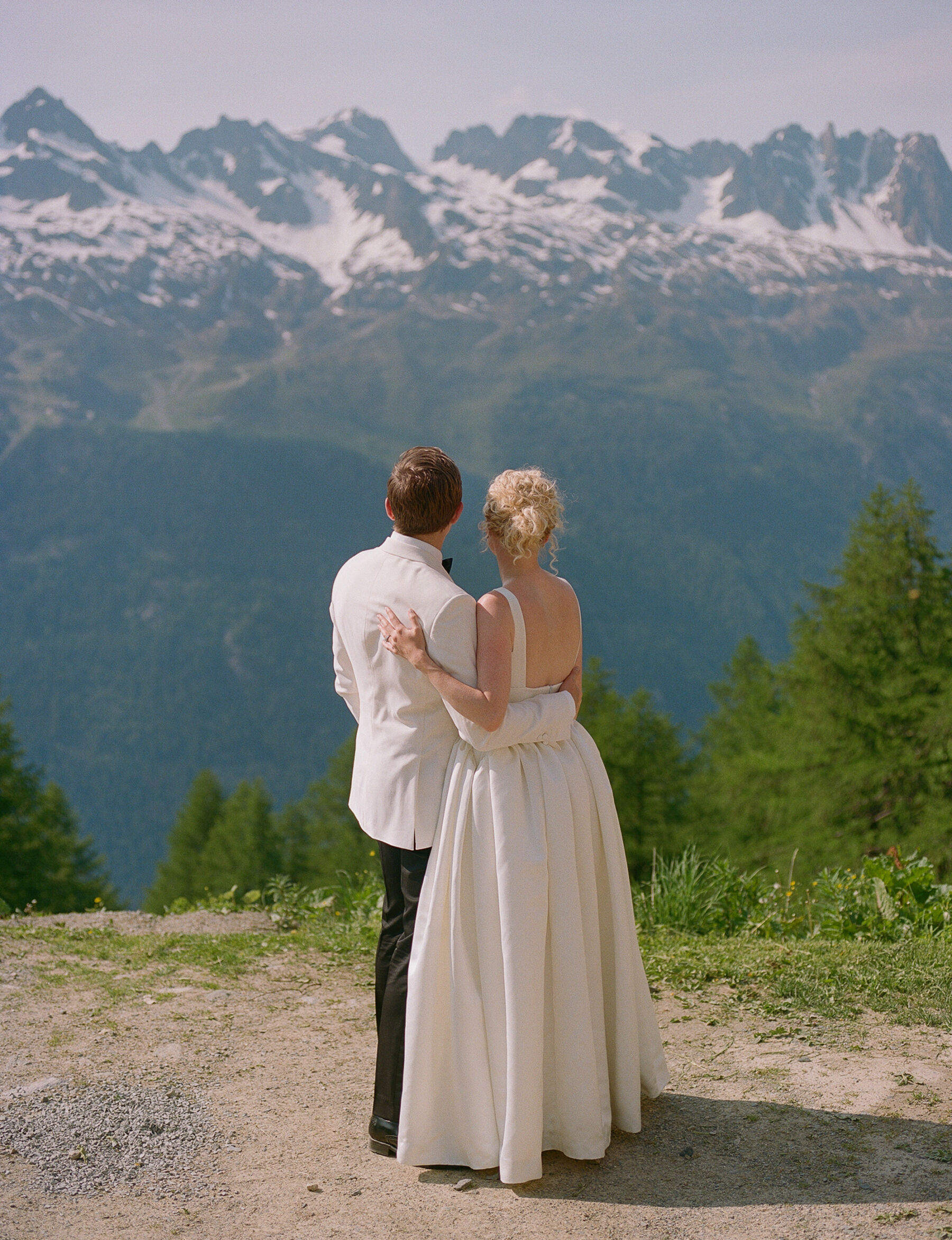 Georgia in Emilia Wickstead, For Her Classy & Elegant Black Tie Mountain Wedding in the Chamonix 26 Bride and groom looking out onto the mountains at Chamonix, France. Bride wears an Emilia Wickstead wedding dress, groom wears a white tuxedo.