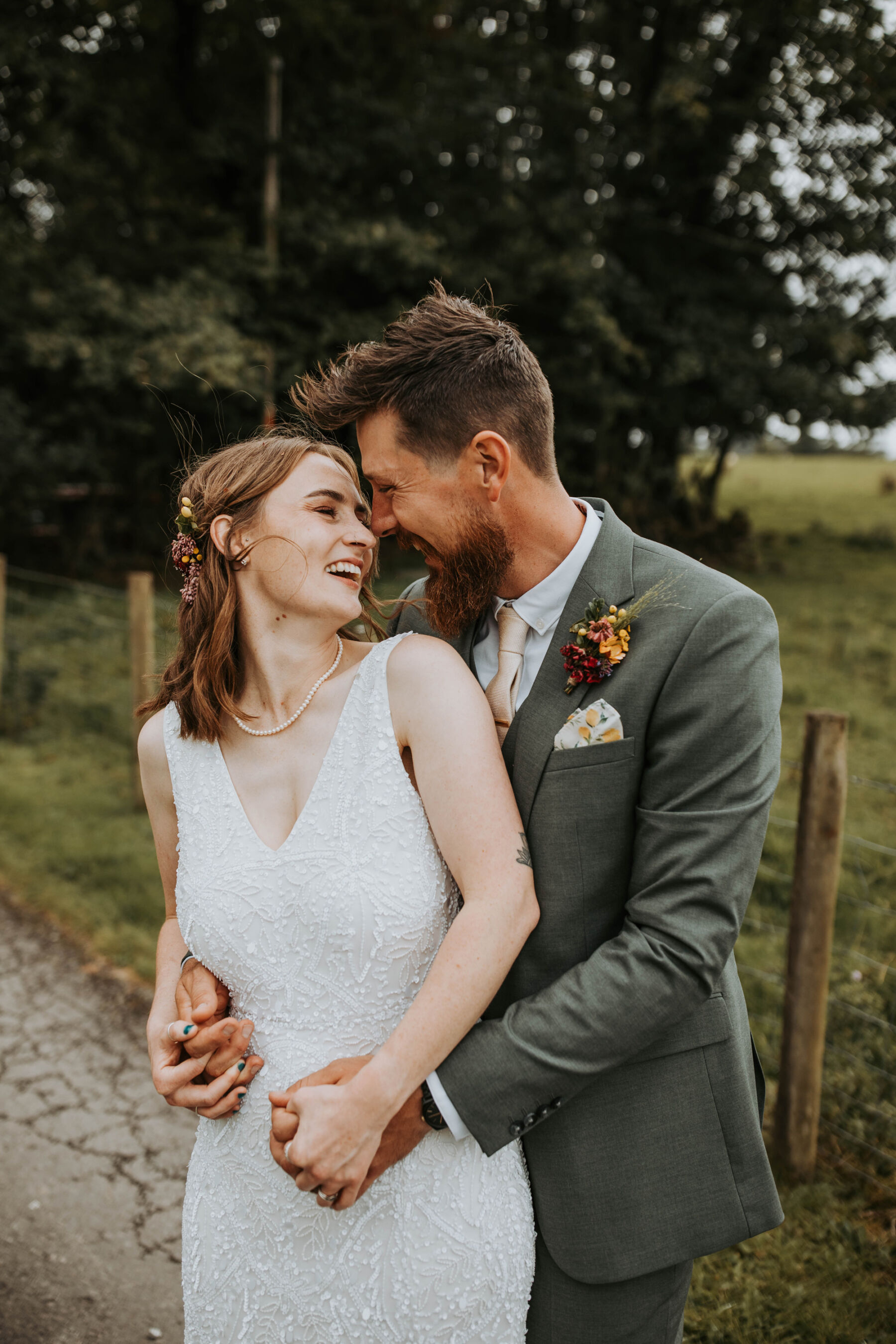 Sophie & Hal's Joyful, Colourful & Sustainable DIY Barn Wedding at Low Hall The Lakes 37 Happy bride and groom embracing whilst having portraits taken after their wedding ceremony. The bride turns her head back to look lovingly into the face of her groom who is gently holding her around her waist. She wears a simple ASOS wedding dress.