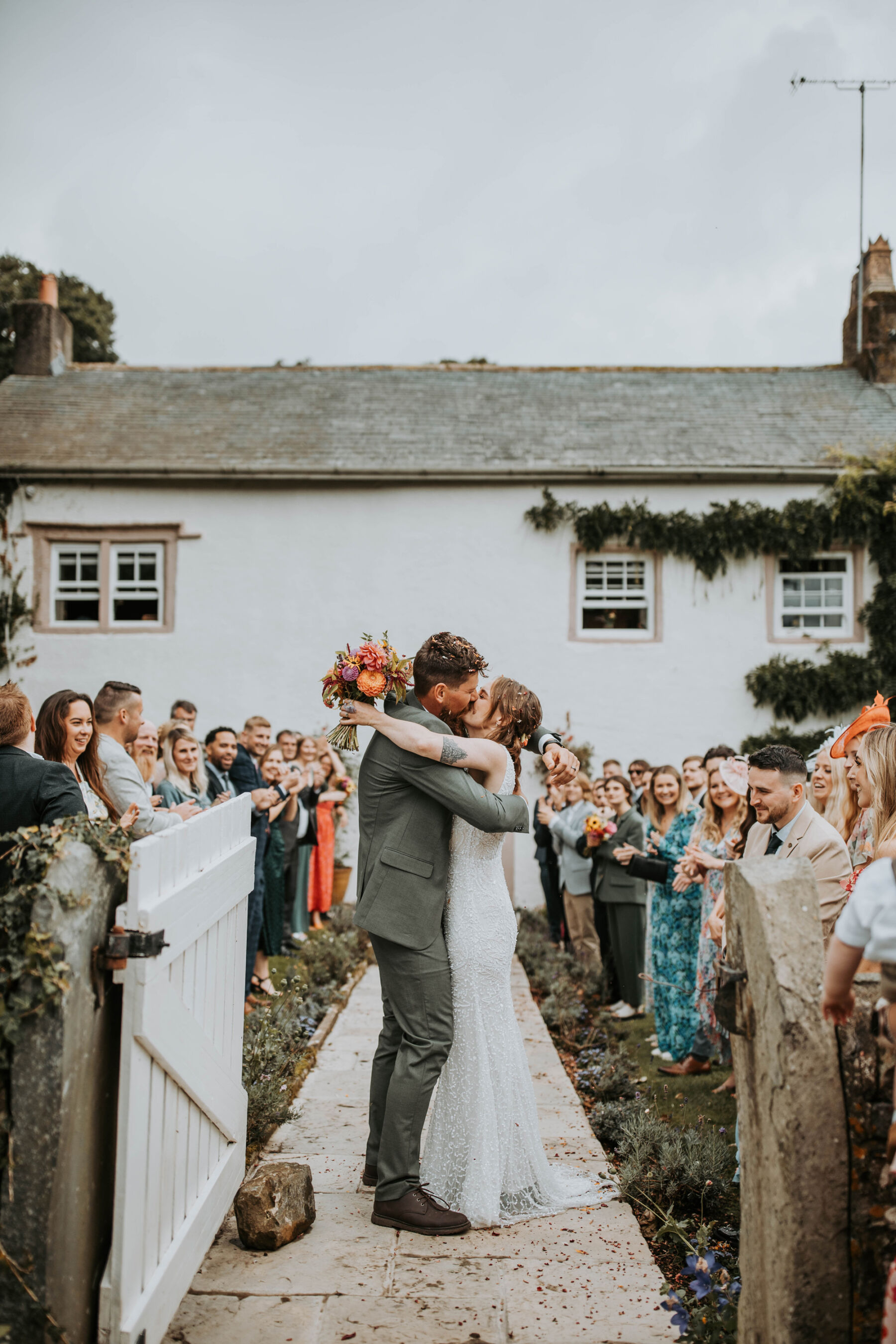 Sophie & Hal's Joyful, Colourful & Sustainable DIY Barn Wedding at Low Hall The Lakes 29 Newlywed bride and groom kissing and embracing outside Low Hall The Lakes, The Lake District.