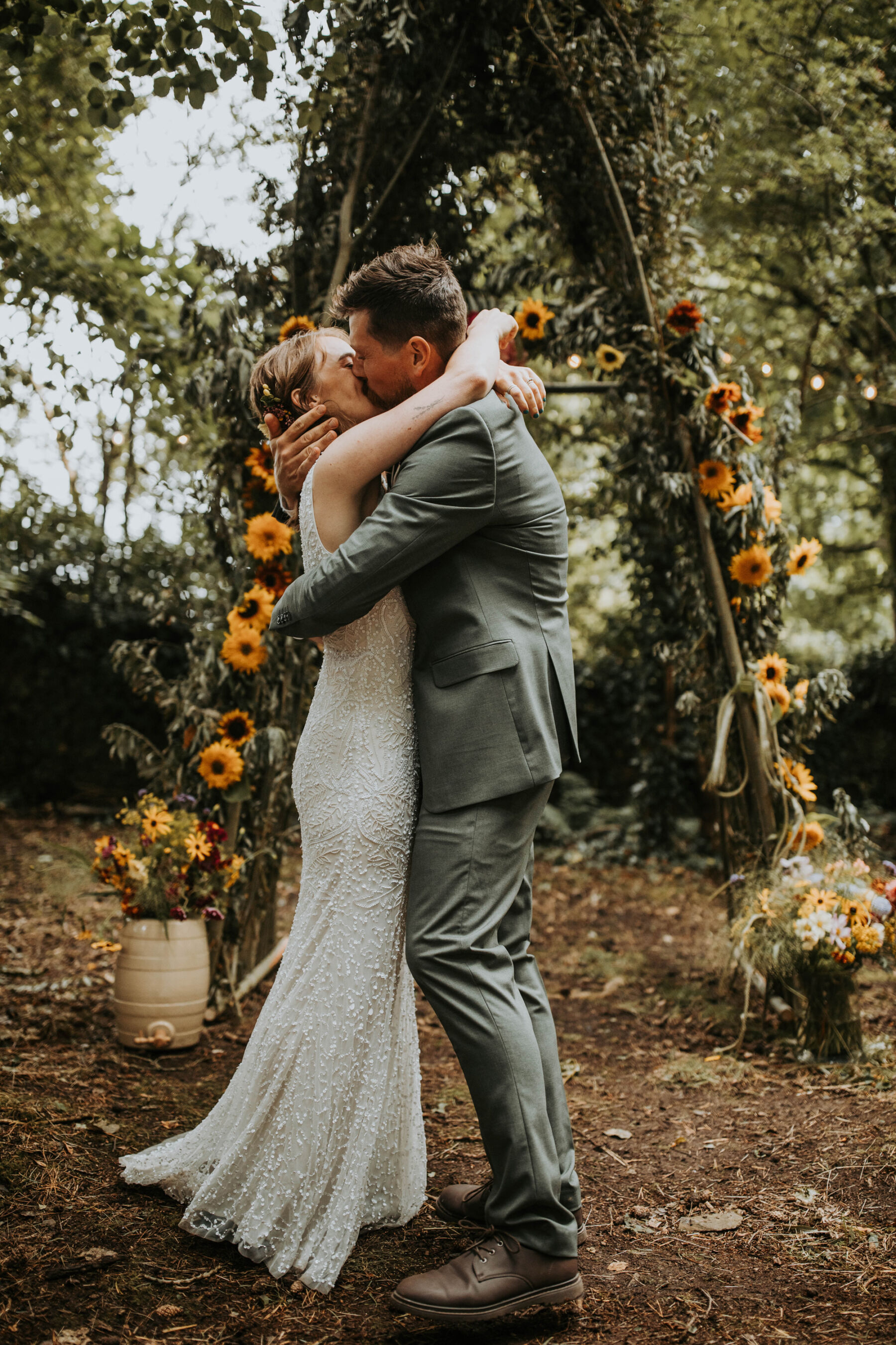 Sophie & Hal's Joyful, Colourful & Sustainable DIY Barn Wedding at Low Hall The Lakes 35 Bride and groom embracing and kissing after being announced man and wife during their outdoor, woodland wedding ceremony at Low Hall The Lakes in The Lake District.