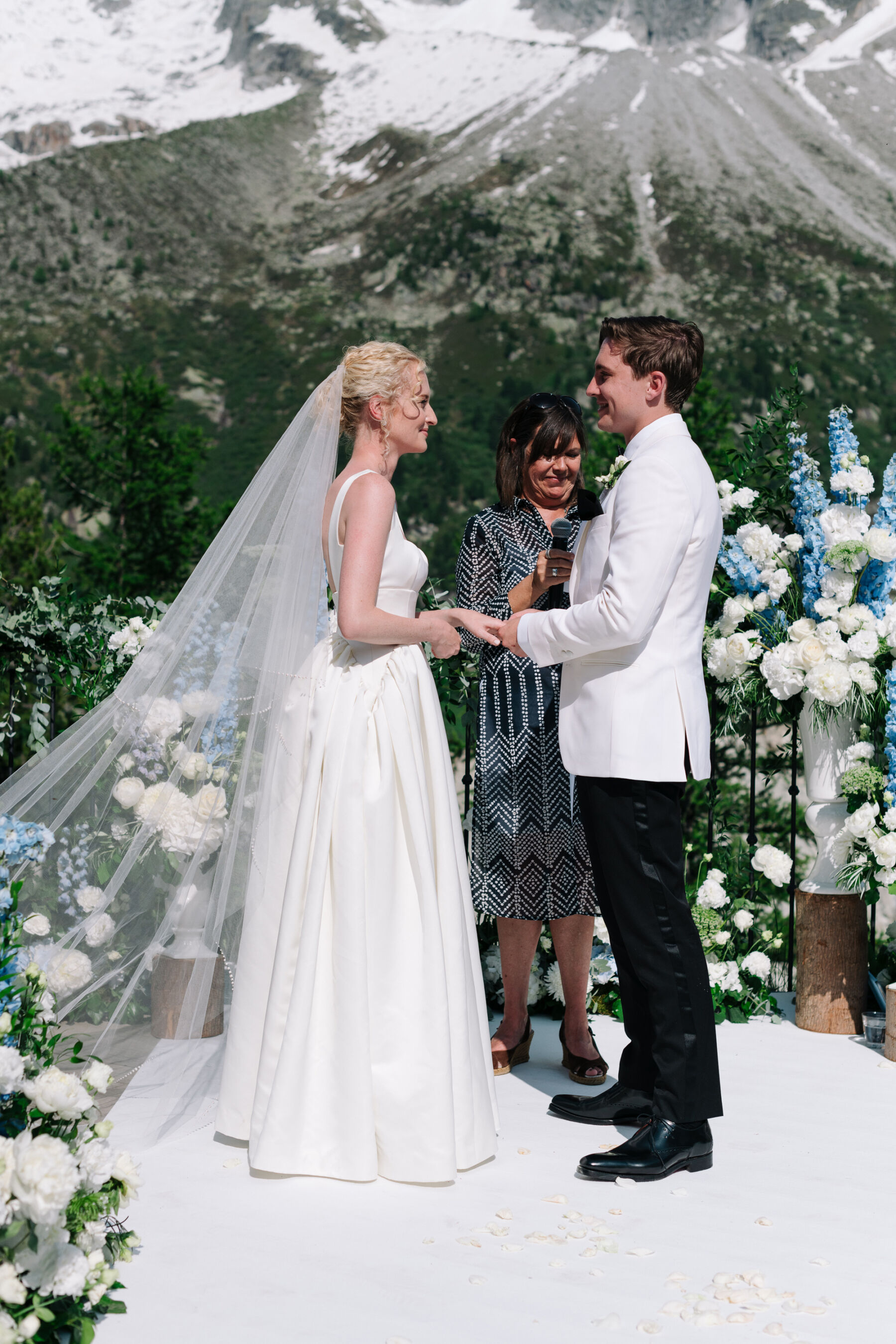 Georgia in Emilia Wickstead, For Her Classy & Elegant Black Tie Mountain Wedding in the Chamonix 24 Outdoor wedding at Mont Blanc in Chamonix France, the mountain rises in the background of the wedding reception. Groom in white tuxedo. Bride in Emilia Wickstead.