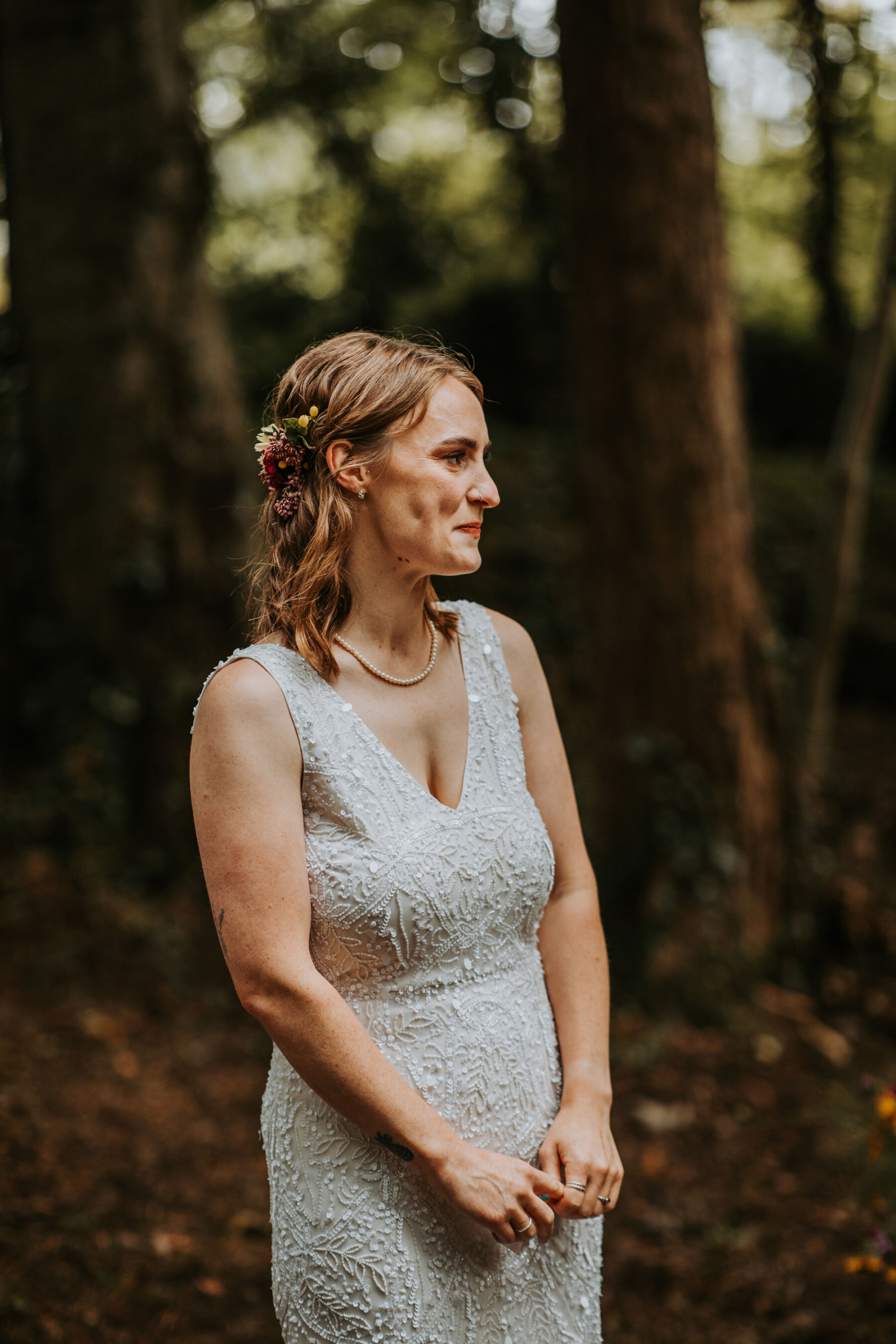 Sophie & Hal's Joyful, Colourful & Sustainable DIY Barn Wedding at Low Hall The Lakes 32 Bride looking emotional during her outdoor wedding ceremony. She has shoulder length loose wavy hair with flowers in the back of her hair keeping her hair off her face. She wears an ASOS wedding dress with sequins.