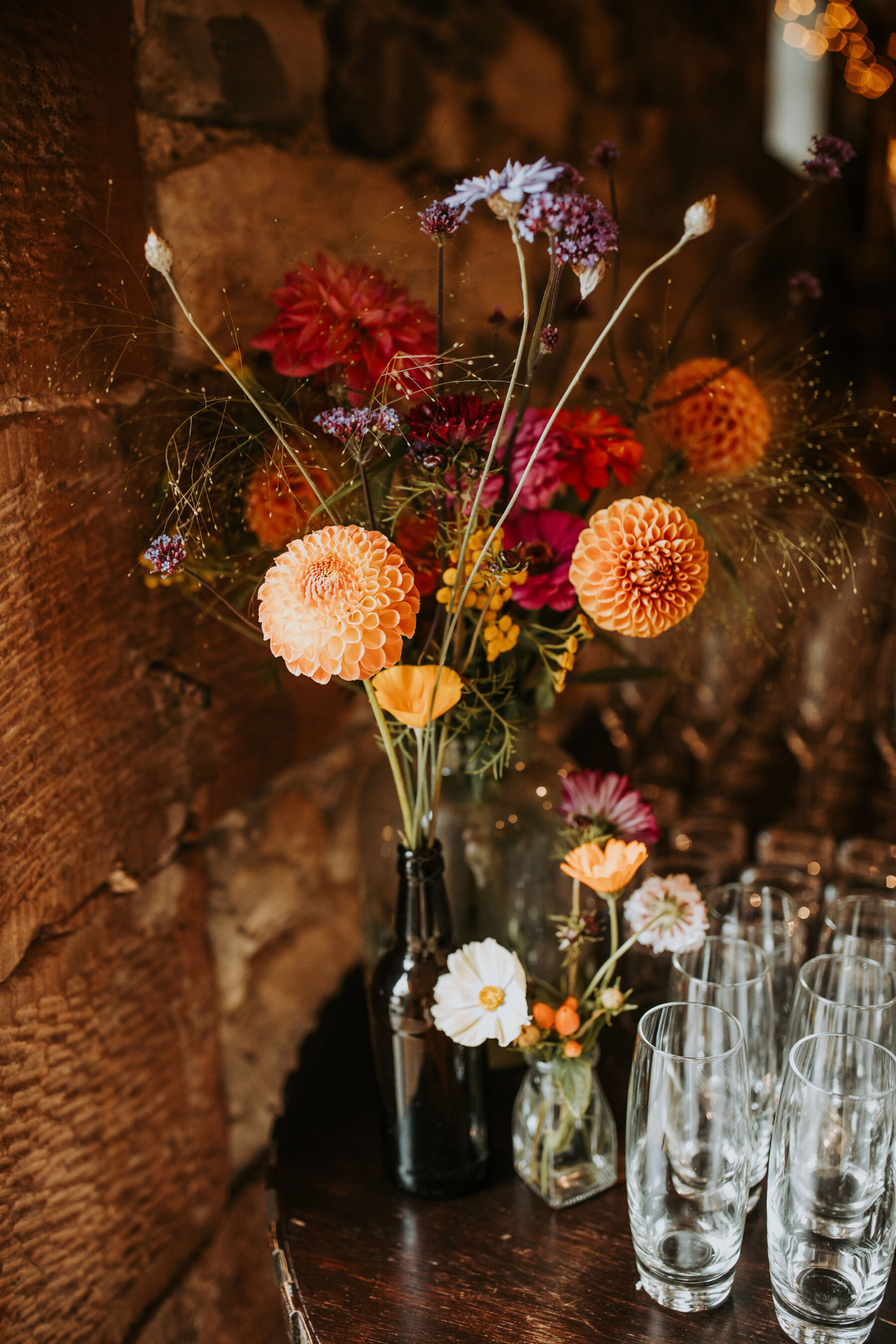 Sophie & Hal's Joyful, Colourful & Sustainable DIY Barn Wedding at Low Hall The Lakes 44 Colourful Dahlia and other wedding flowers in a recycled glass bottle for a DIY wedding in a barn.