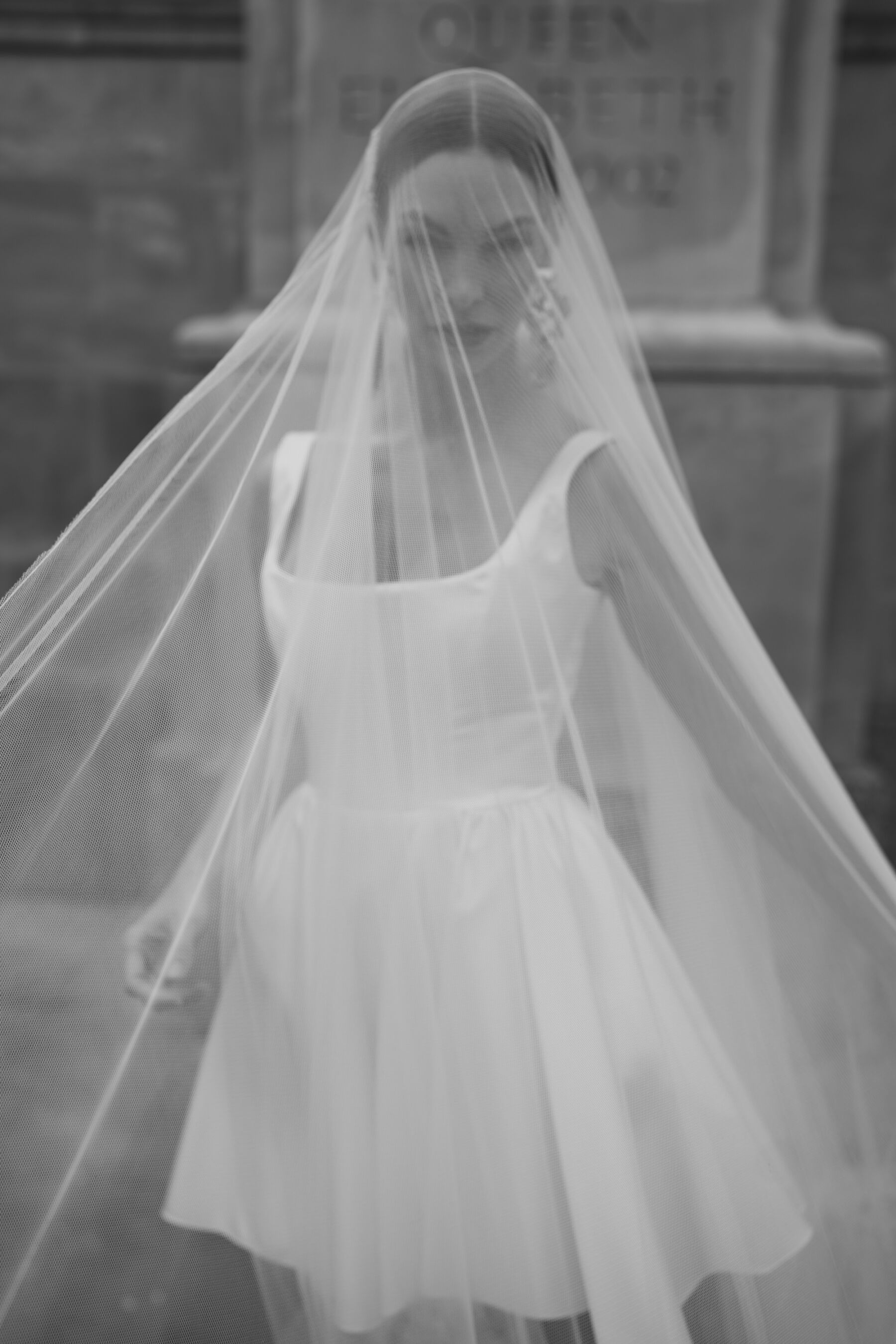 Cool black and white photograph of a bride wearing large gold statement earrings and a cute and playful, short wedding dress by Halfpenny London.