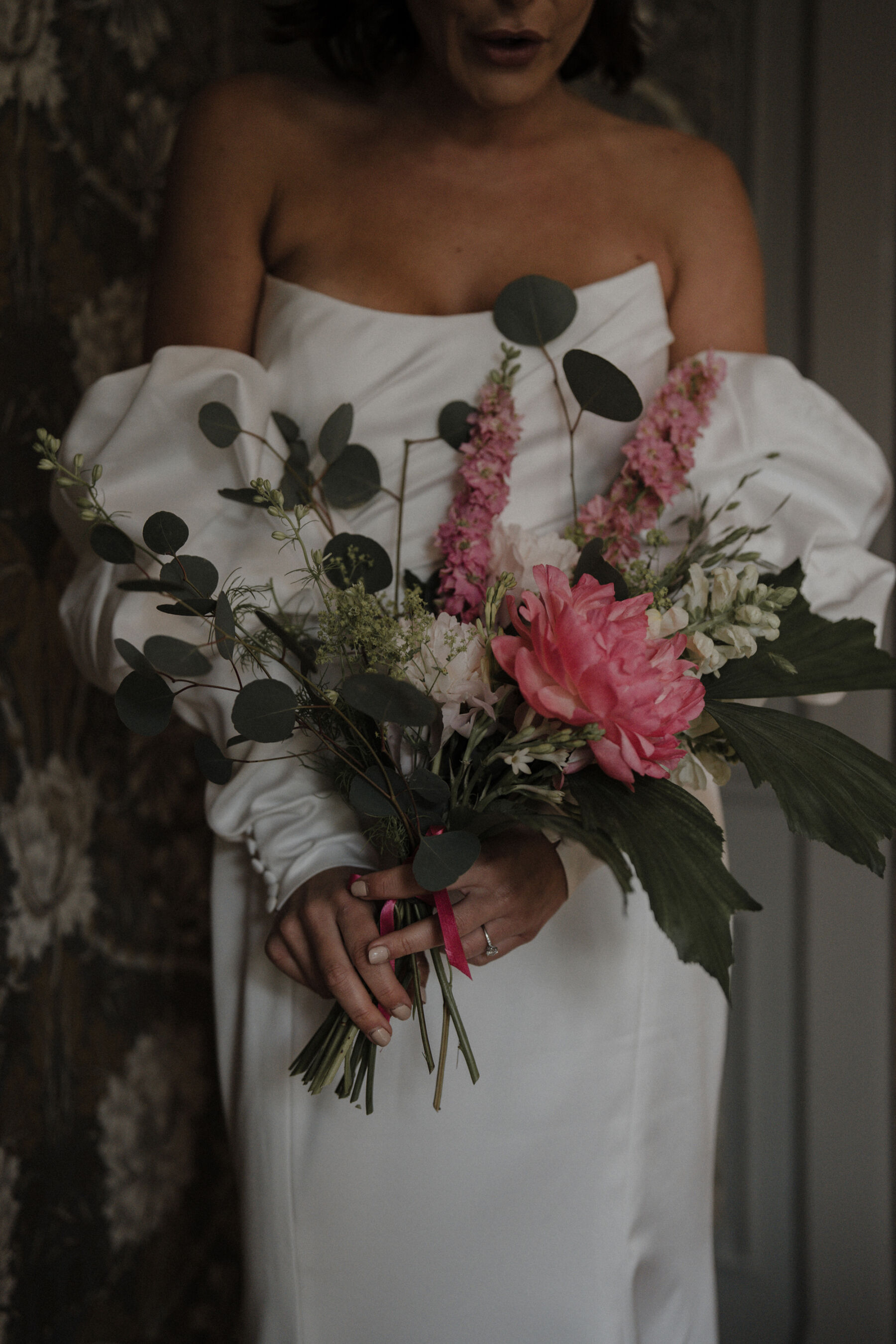 Watters long sleeved modern contemporary wedding dress with bride holding a bouquet with a large peony.