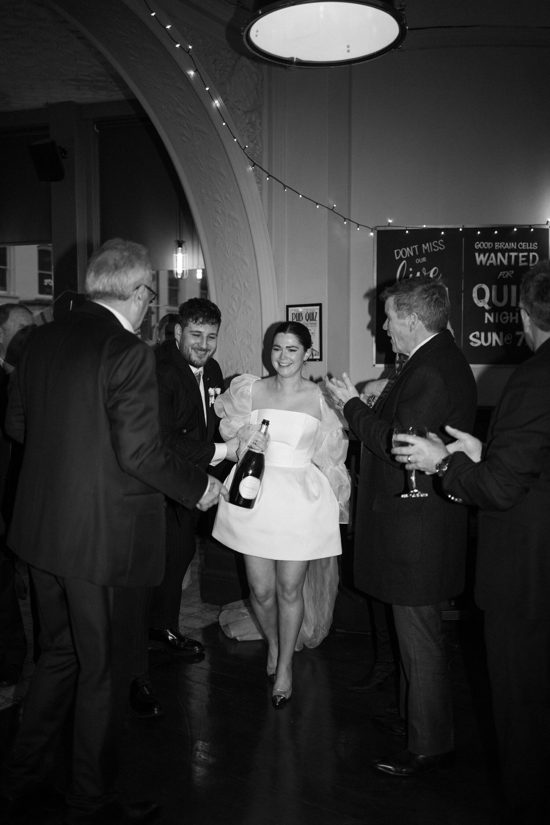 Maddy & Nik’s Cosy and Intimate Winter Wedding with a Custom Jesus Peiro Gown 36 Bride and groom arriving at their evenign reception at The Cellar Taps pub, London. Bride wears a mini dress by Jesus Peiro.