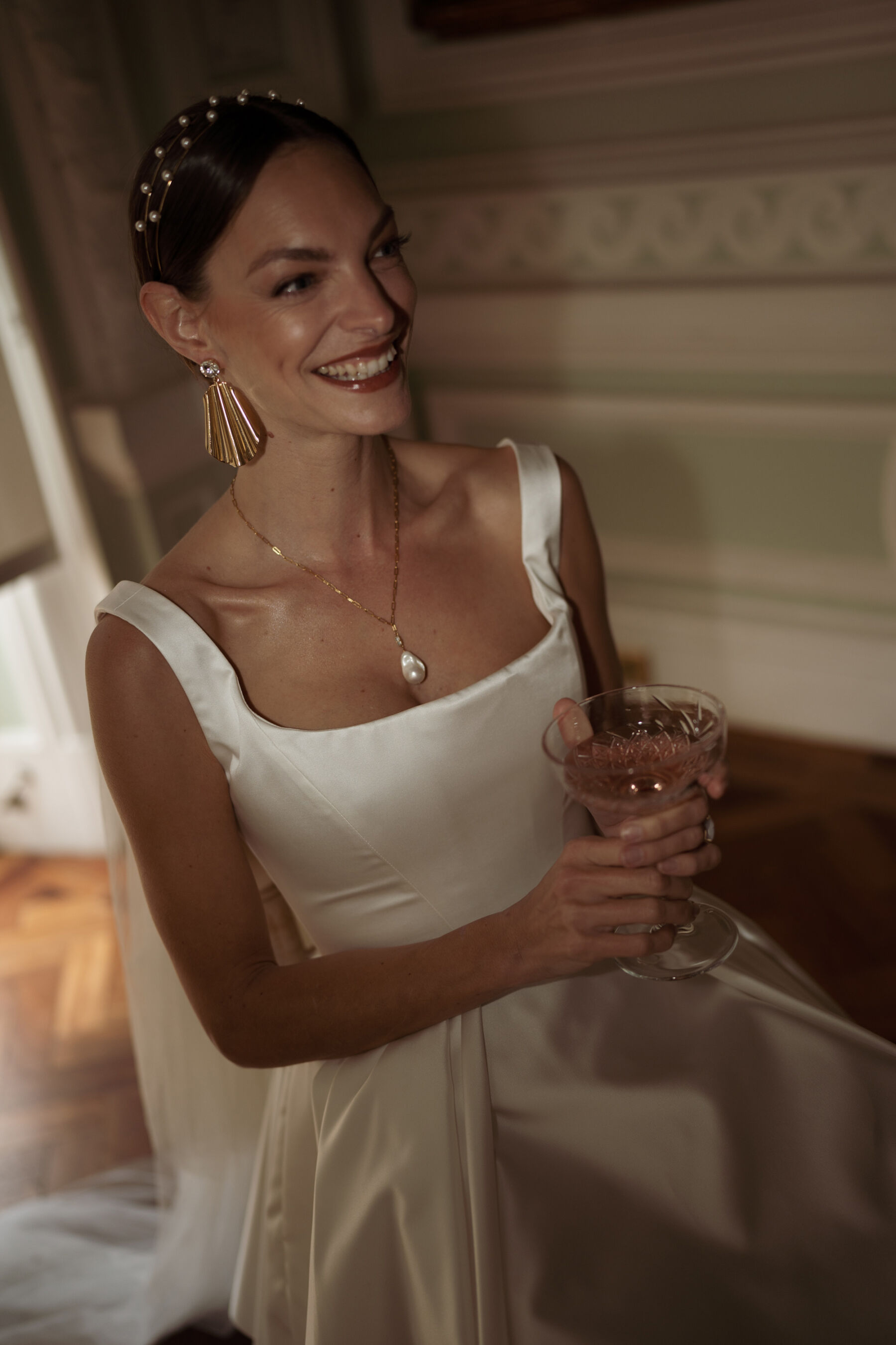 Bride in a short and playful wedding dress by Halfpenny London, holding a champagne coupe and wearing statement gold earrings.