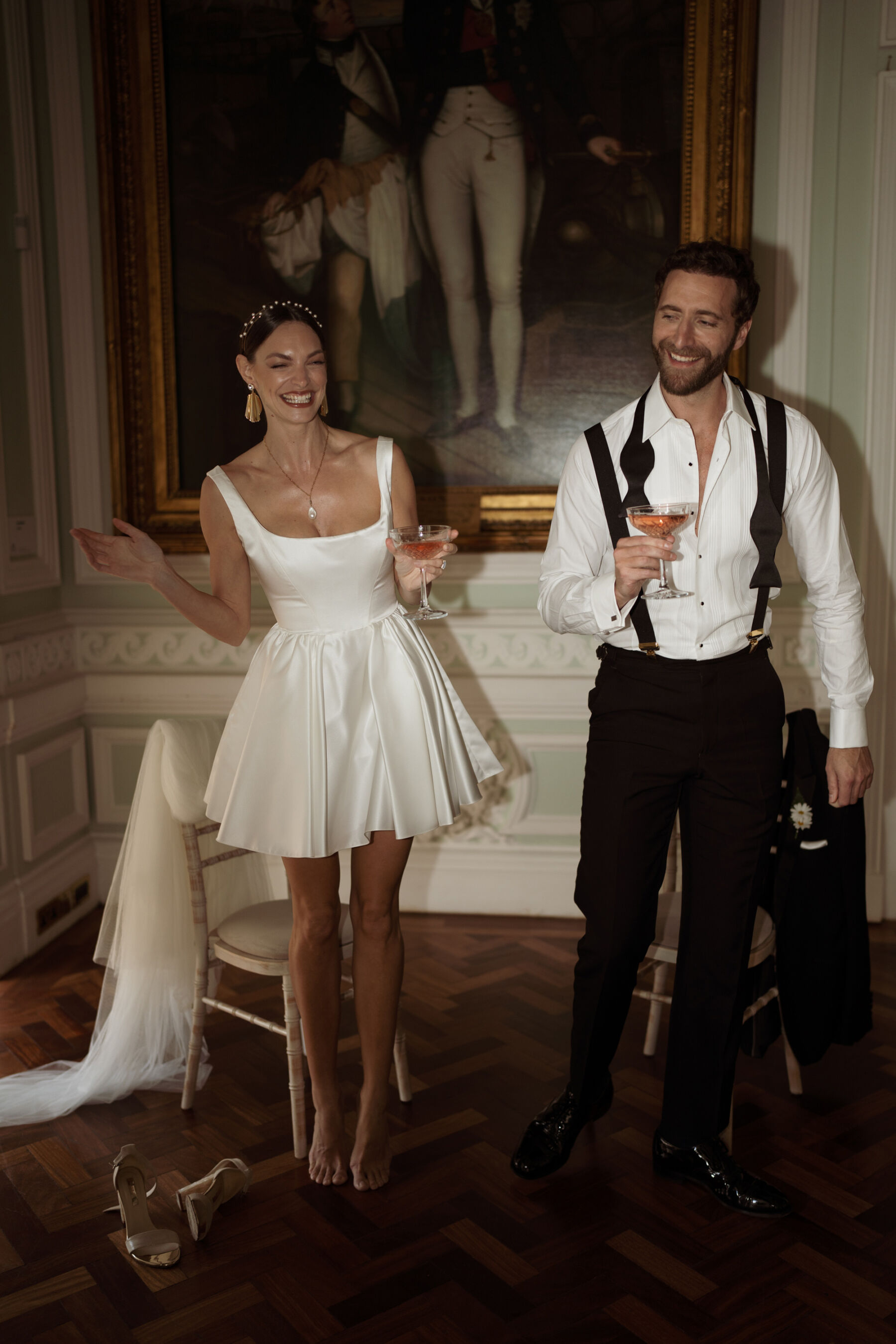 Groom in black tie with his bow tie undone and his shirt unbuttoned, with bride in a short and playful wedding dress by Halfpenny London.