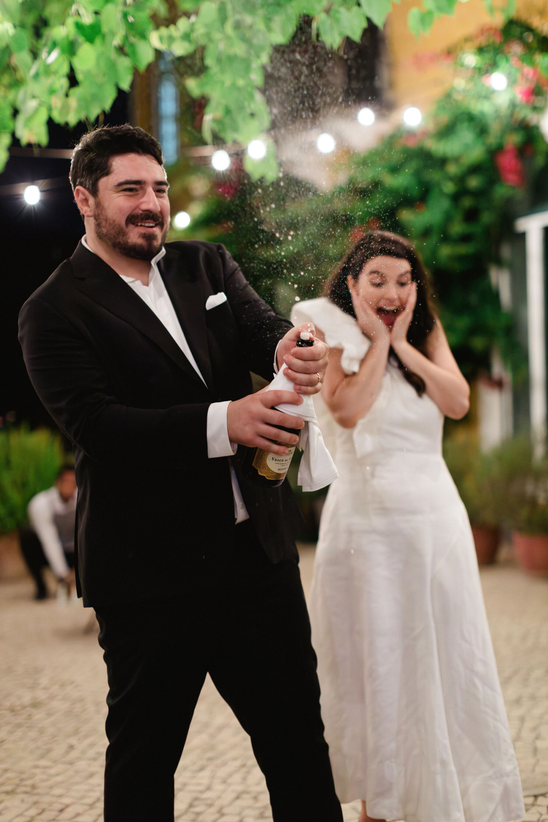 Olivia & Tim's Classy & Elegant Vineyard Wedding in Portugal 41 Groom popping a bottle of champagne and bride clutching her cheeks in delight as the champagne sprays.
