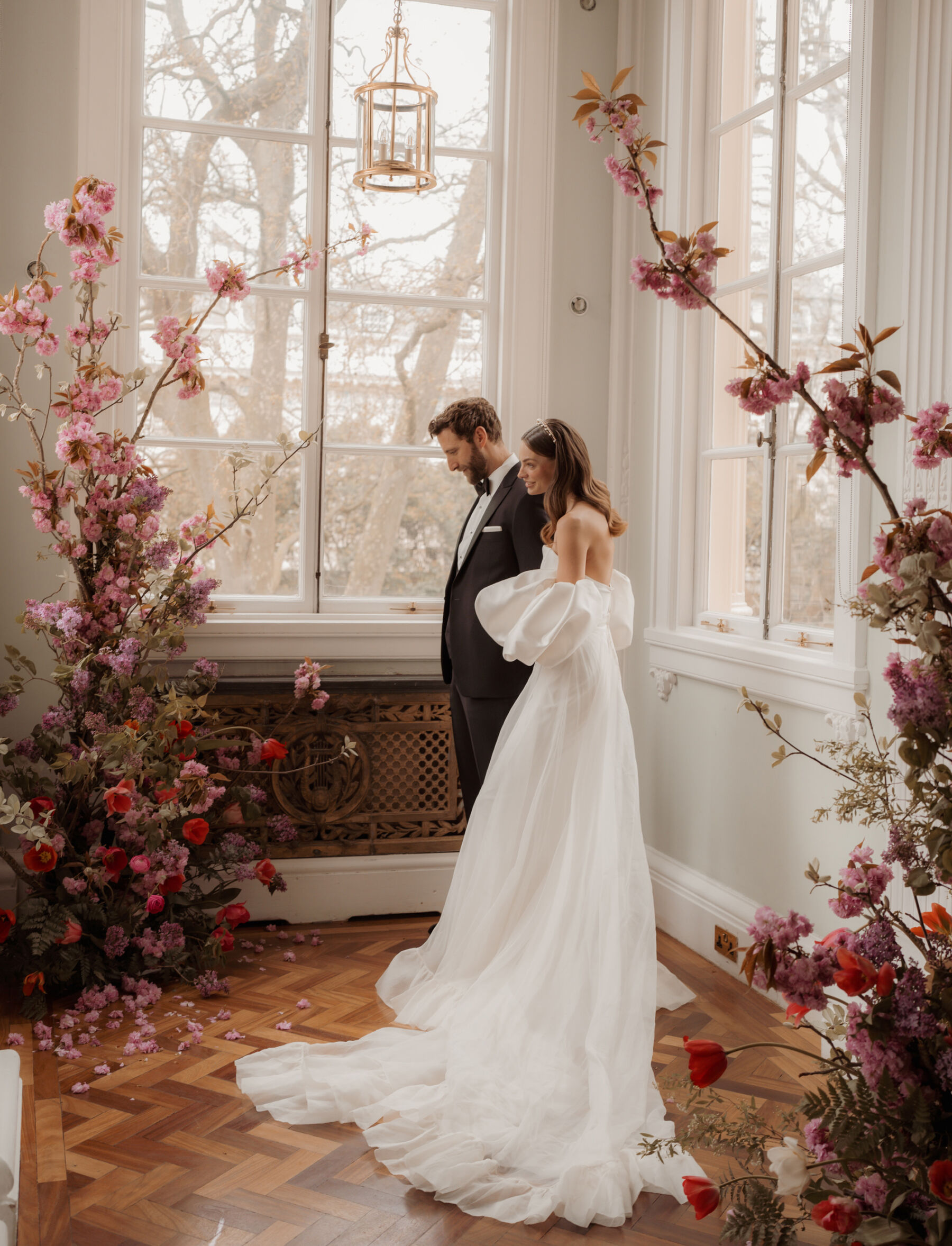 Bride seated next to a broken floral arch with Spring cherry blossom and Icelandic poppies. Romantic wedding dress by Halfpenny London at 10-11 Carlton Terrace London. Car Arwel Photography.