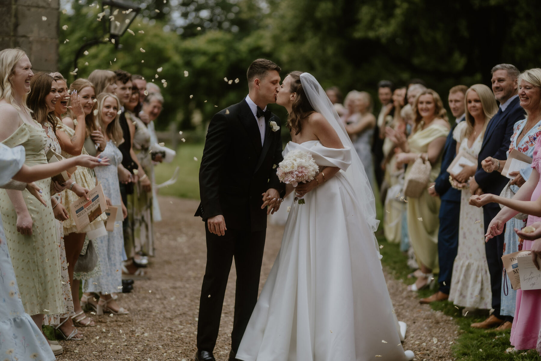 An Investment Banker & Her Prestwold Hall Wedding, with a Milla Nova Gown & Berta Legging Boots 24 Bride and groom embracing in a confetti shower outside the church. She carries a pastel
