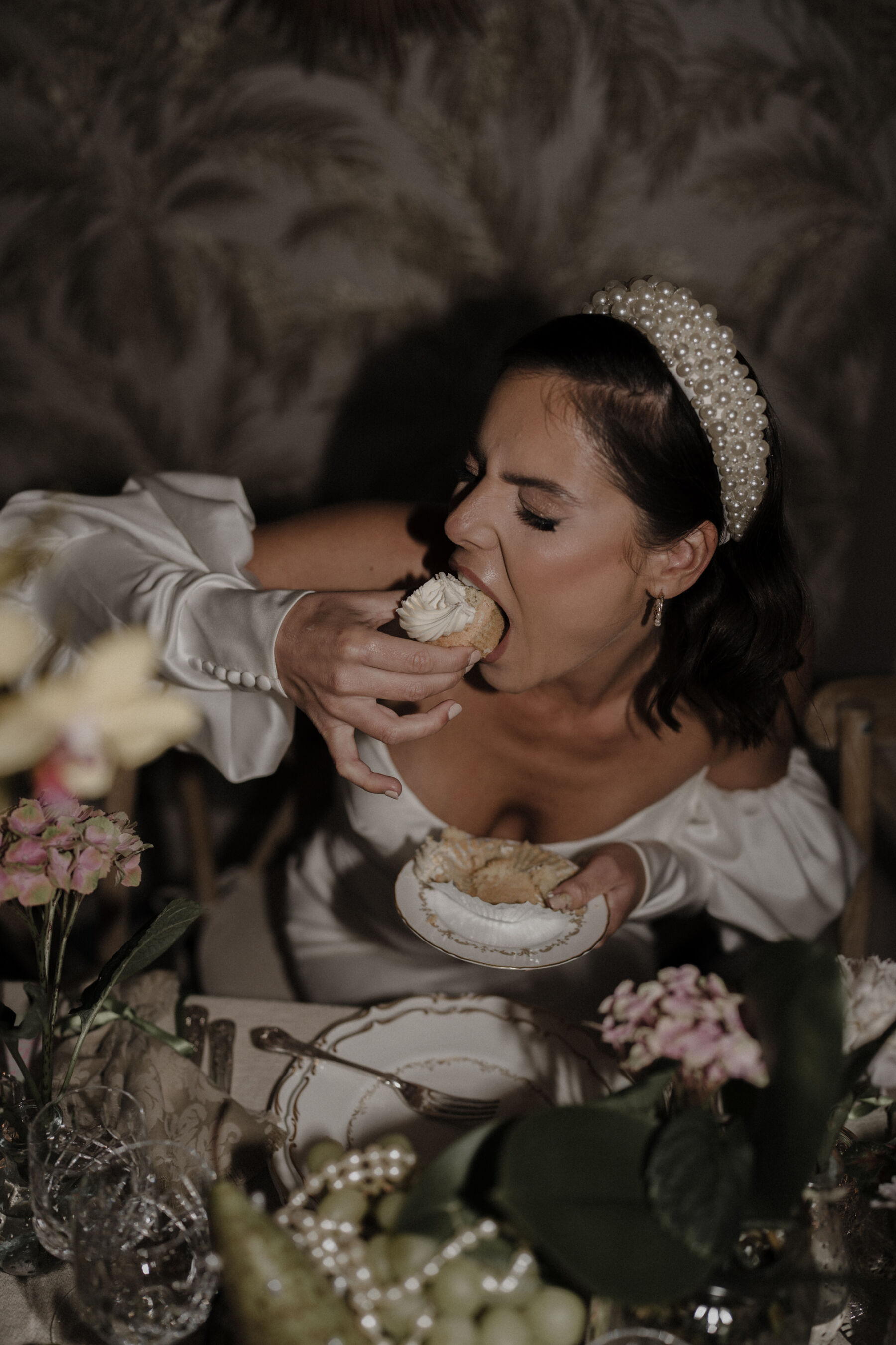 Bride tucking in to a wedidng cupcake - she is wearing a pearl headband and Watters wedding dress with pearls on the cuff.
