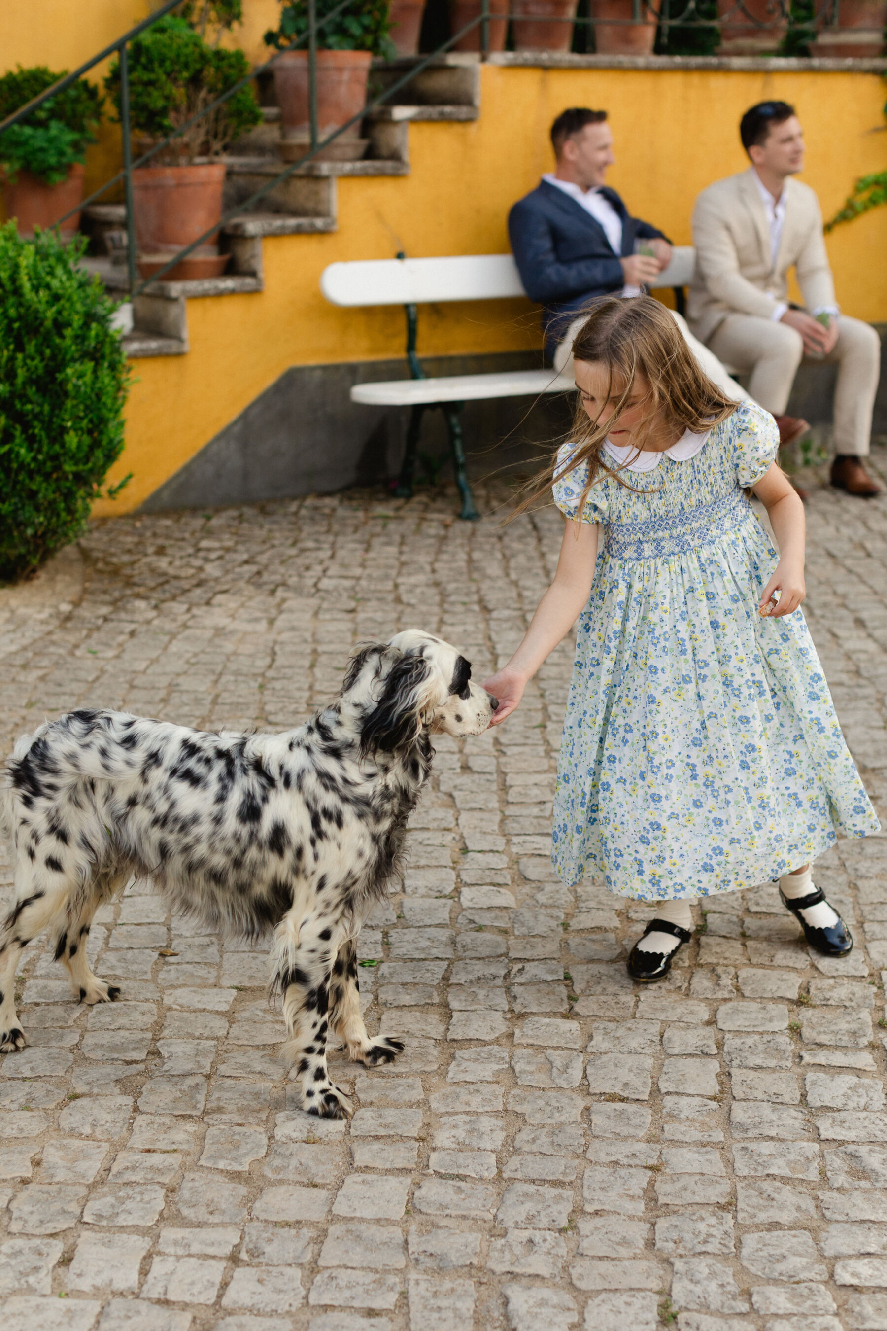 Olivia & Tim's Classy & Elegant Vineyard Wedding in Portugal 36 Little flower girl stroking a dog in the street at a wedding in Portugal.