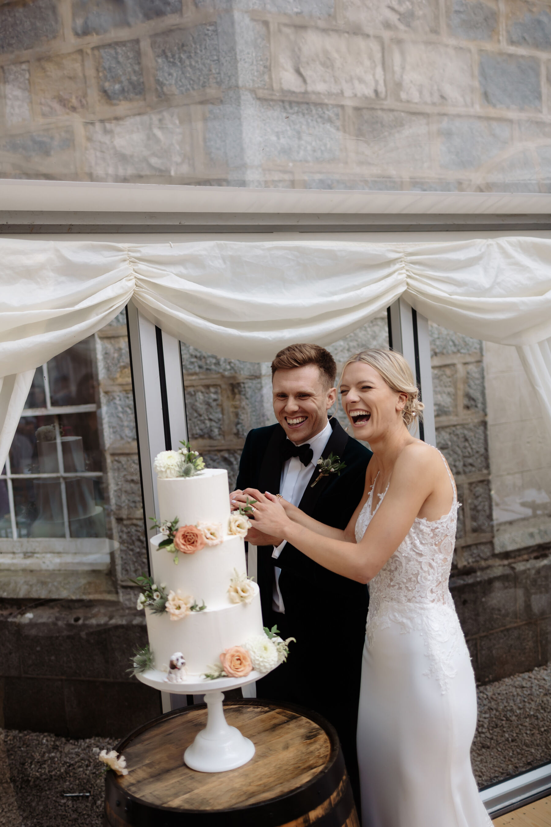 Emily in Rosa Clara for her Romantic & Elegant July Wedding at Cluny Castle 36 Bride and groom cutting their 3 tier wedding cake with peach flowers.