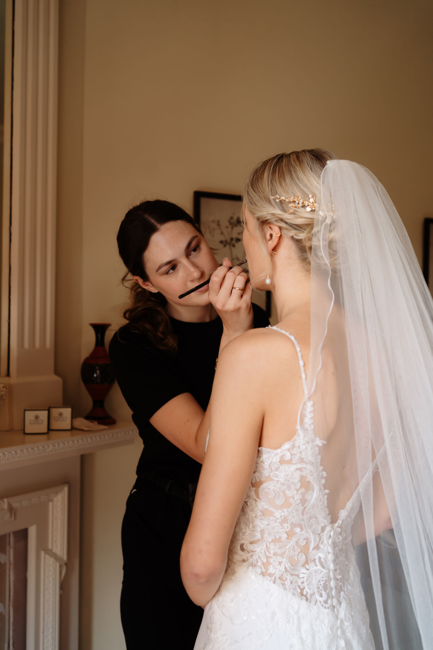 Emily in Rosa Clara for her Romantic & Elegant July Wedding at Cluny Castle 17 Bride wearing Rosa Clara wedding dress, a gold floral bridal headpiece and having her lipstick applied by a makeup artist.