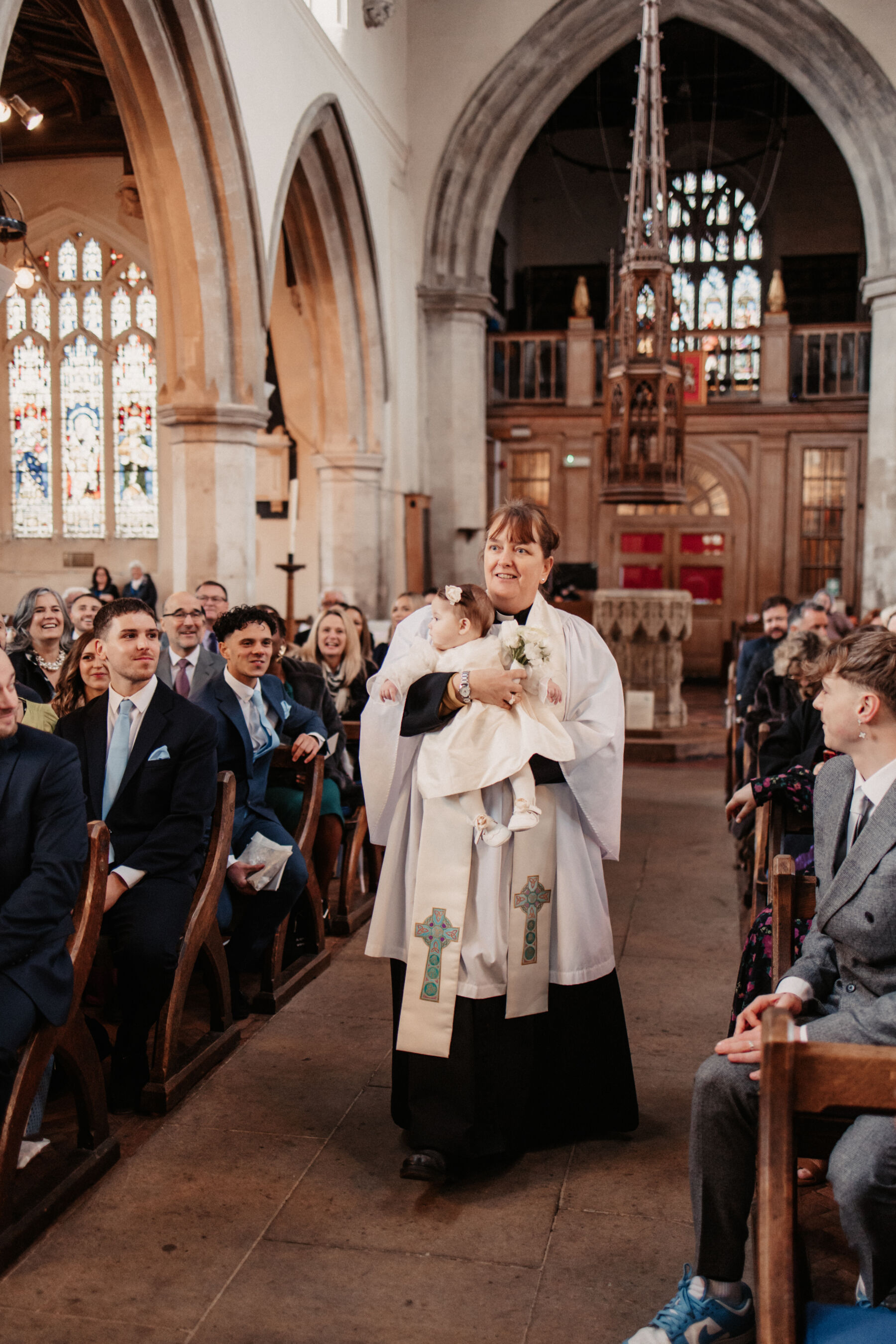 Maddy & Nik’s Cosy and Intimate Winter Wedding with a Custom Jesus Peiro Gown 12 Female vicar walking down the aisle with a sweet baby girl
