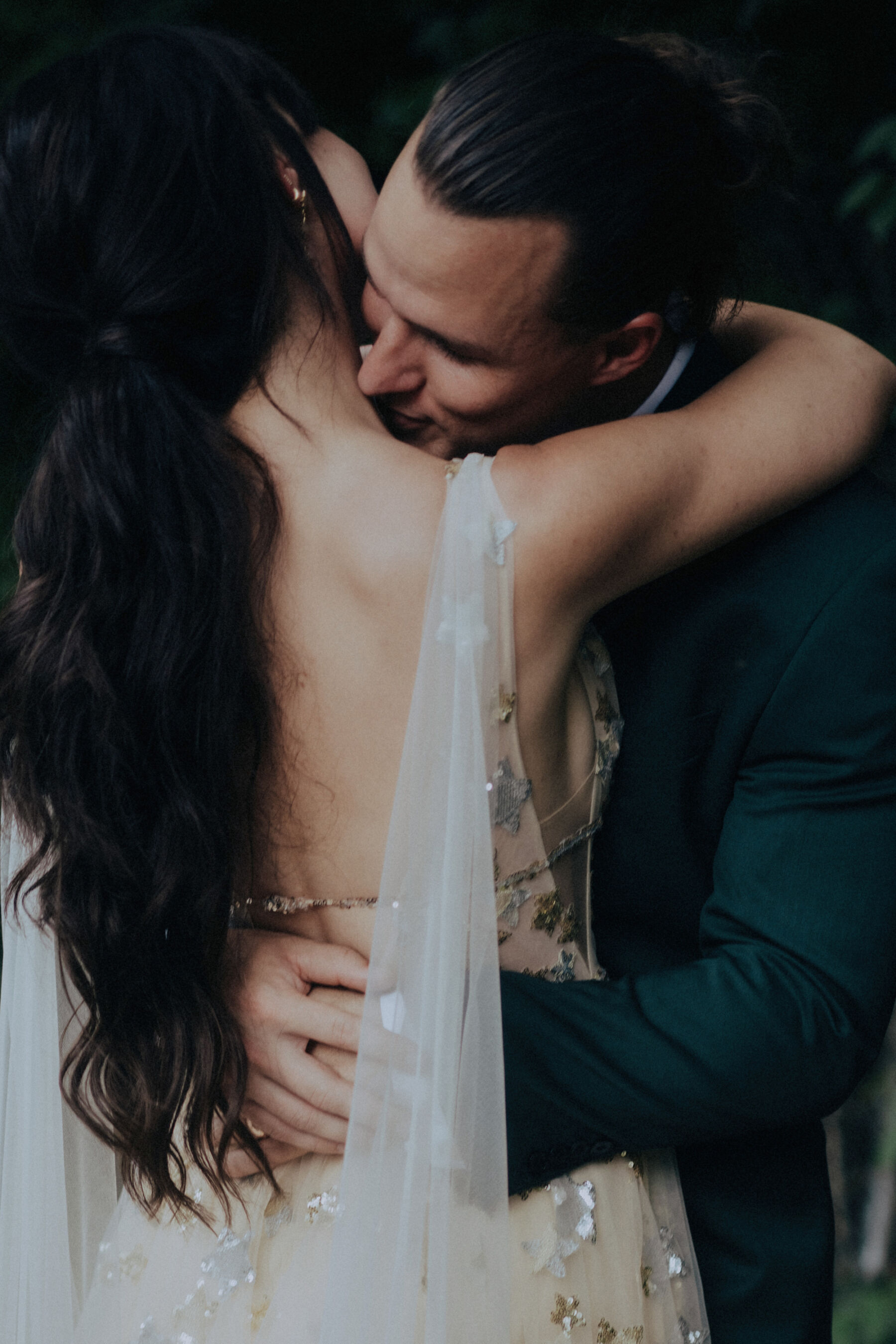 Romantic bride and groom portrait as he leans into her neck to kiss her and she holds him around the shoulders.