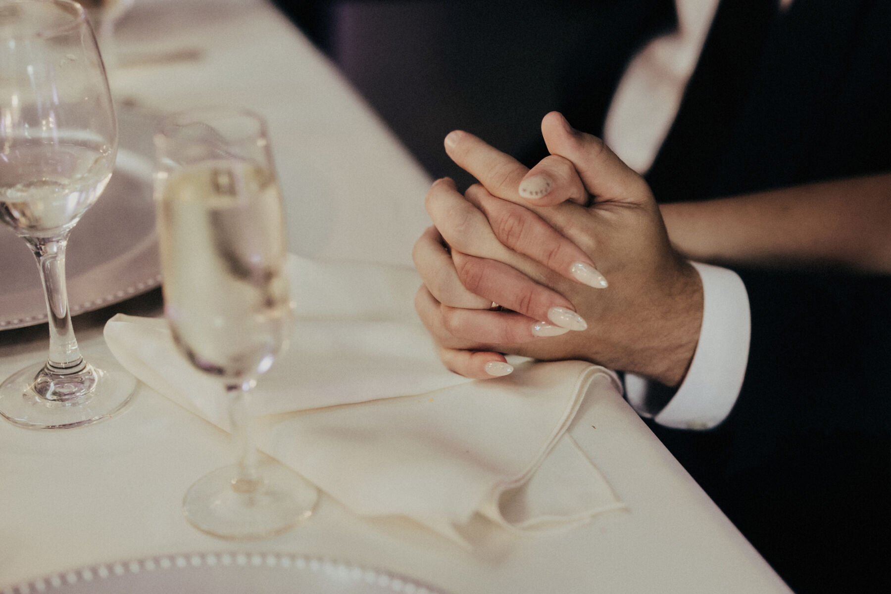 Close up shot of bride and groom interlinking fingers. 