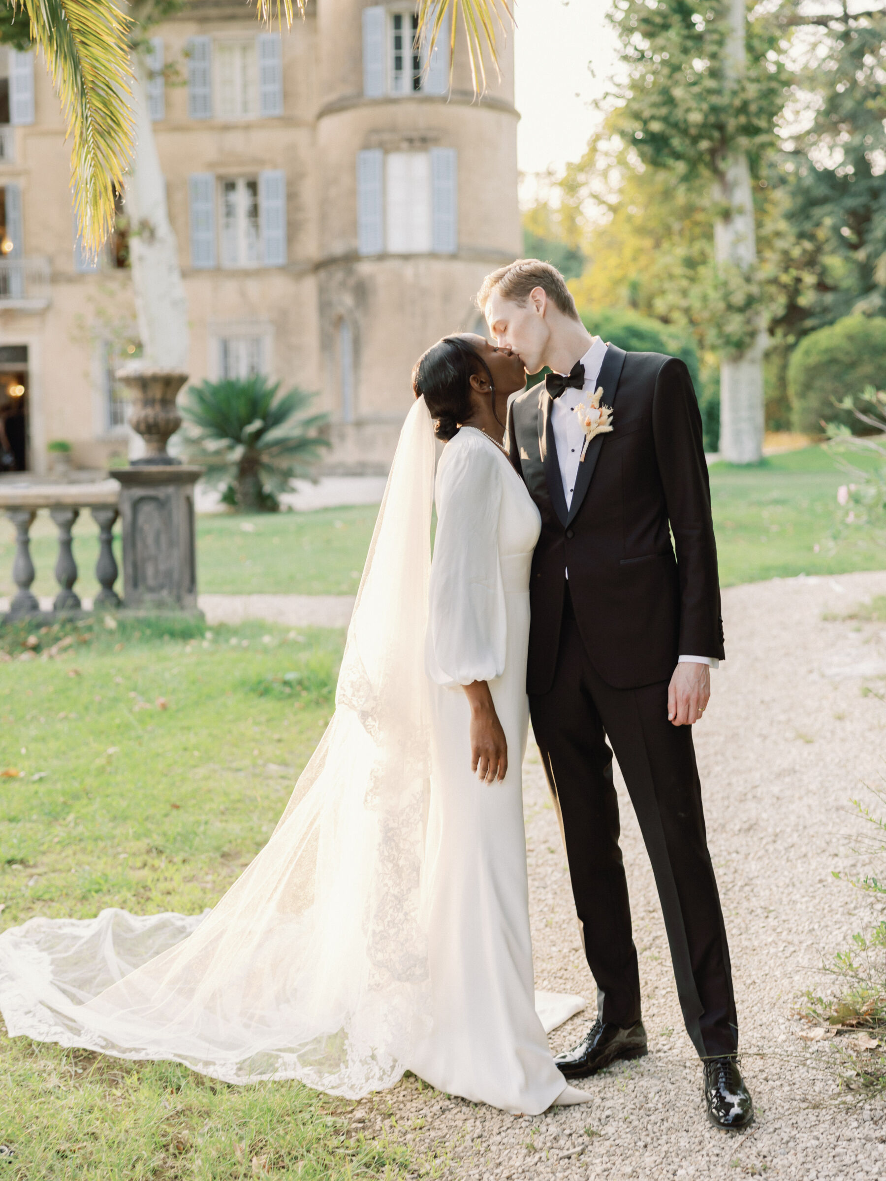 French Riviera Chic Wedding at Château Robernier, Provence, with Lawyer Chanel in Sassi Holford 24 Black bride wearing sassi Holford and kissing her groom who wears black tie. Wedding at Chateau Robernier in Cotignac, Provence, France. Sébastien Boudot Photography.