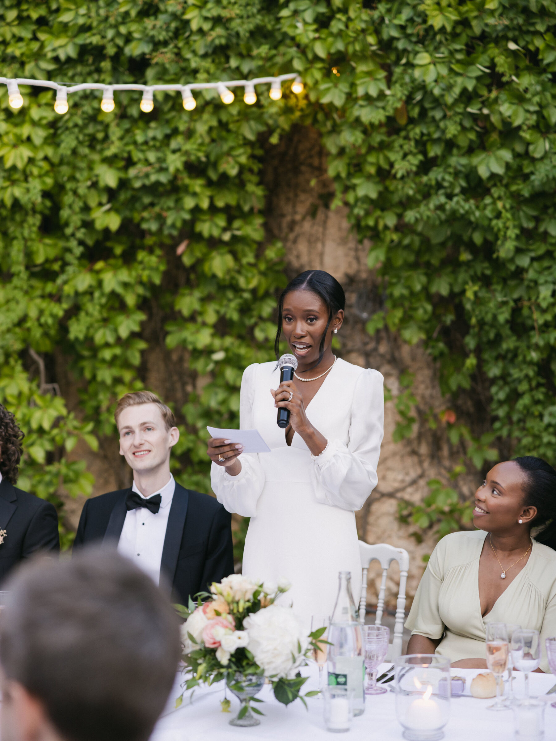 French Riviera Chic Wedding at Château Robernier, Provence, with Lawyer Chanel in Sassi Holford 35 Black bride standing at the reception table to give a speech. Wedding at Chateau Robernier in Cotignac, Provence, France. Sébastien Boudot Photography.