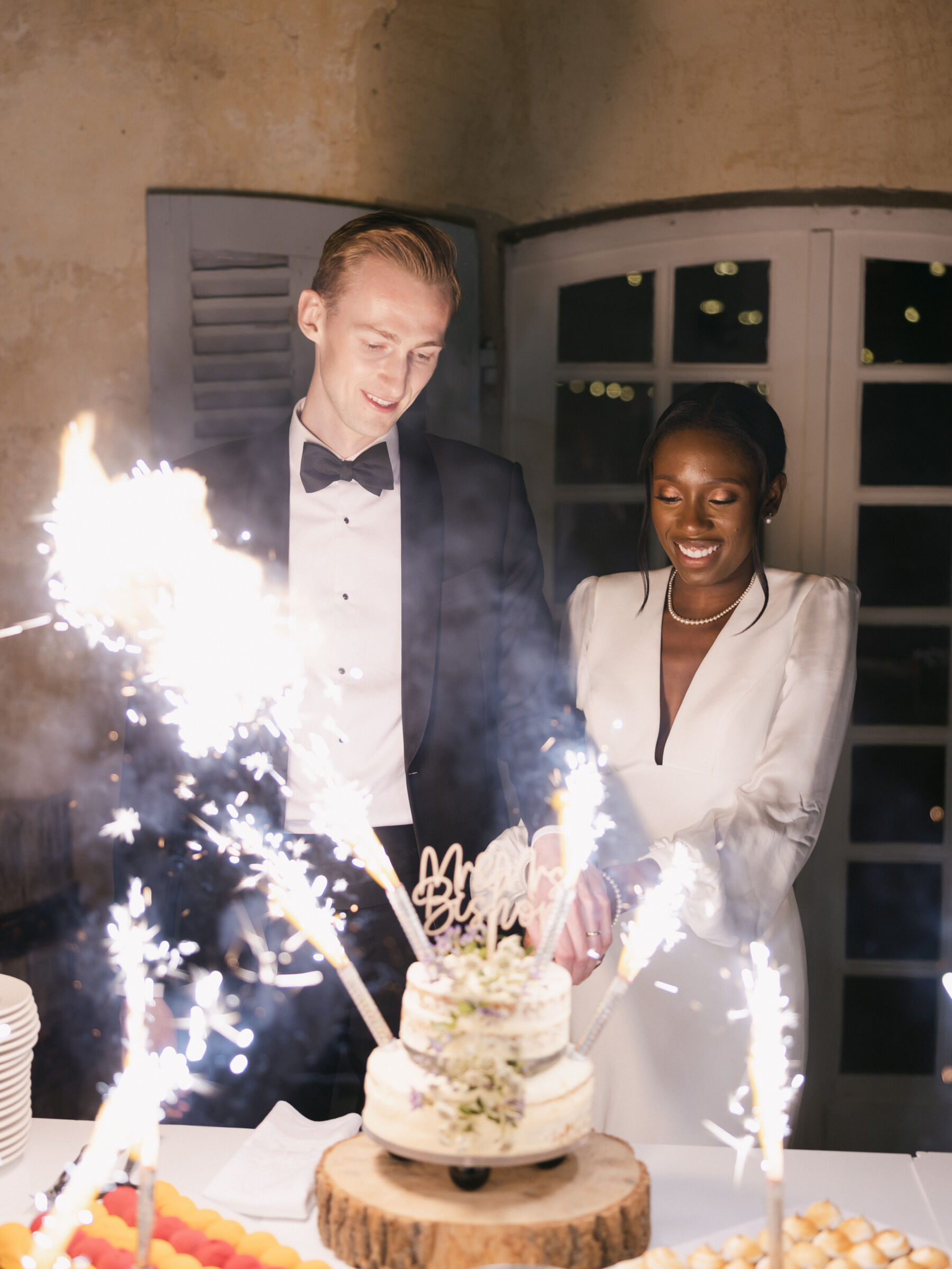 French Riviera Chic Wedding at Château Robernier, Provence, with Lawyer Chanel in Sassi Holford 38 Black bride in Sassi Holford and groom in black tie cutting their wedding which is lit up by wedding sparklers. Wedding at Chateau Robernier in Cotignac, Provence, France. Sébastien Boudot Photography.