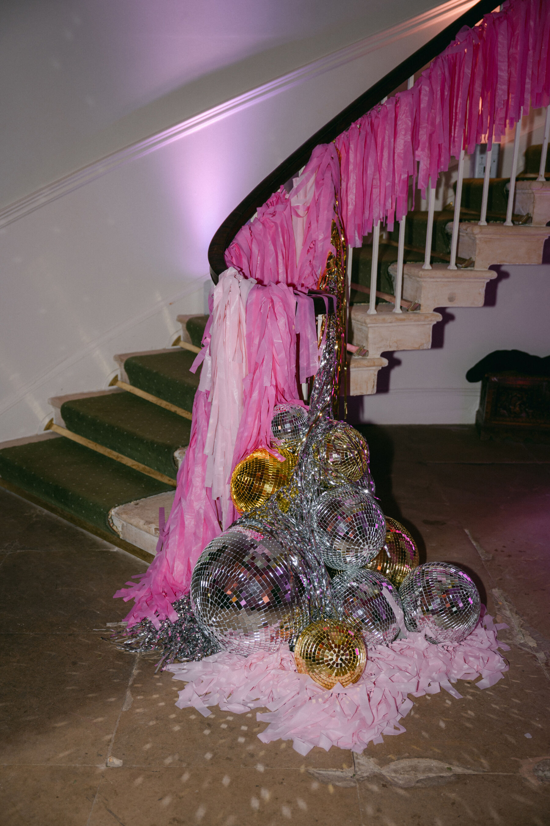 Sweeping curved staircase decorated with pink tassels and mountain of disco balls at Middleton Lodge.