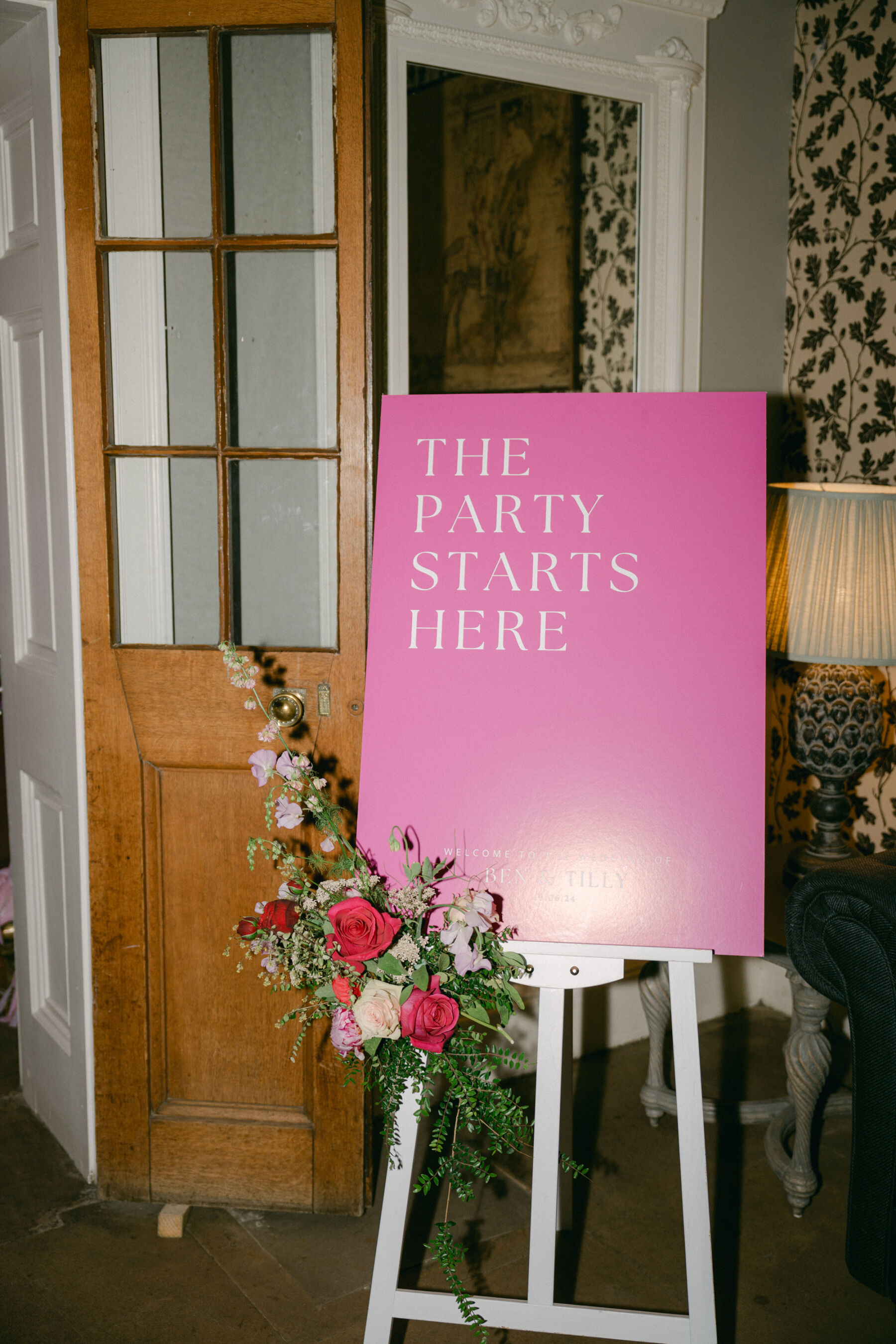 Bright pink wedding sign on a white easel that reads 'THE PARTY STARTS HERE'. 