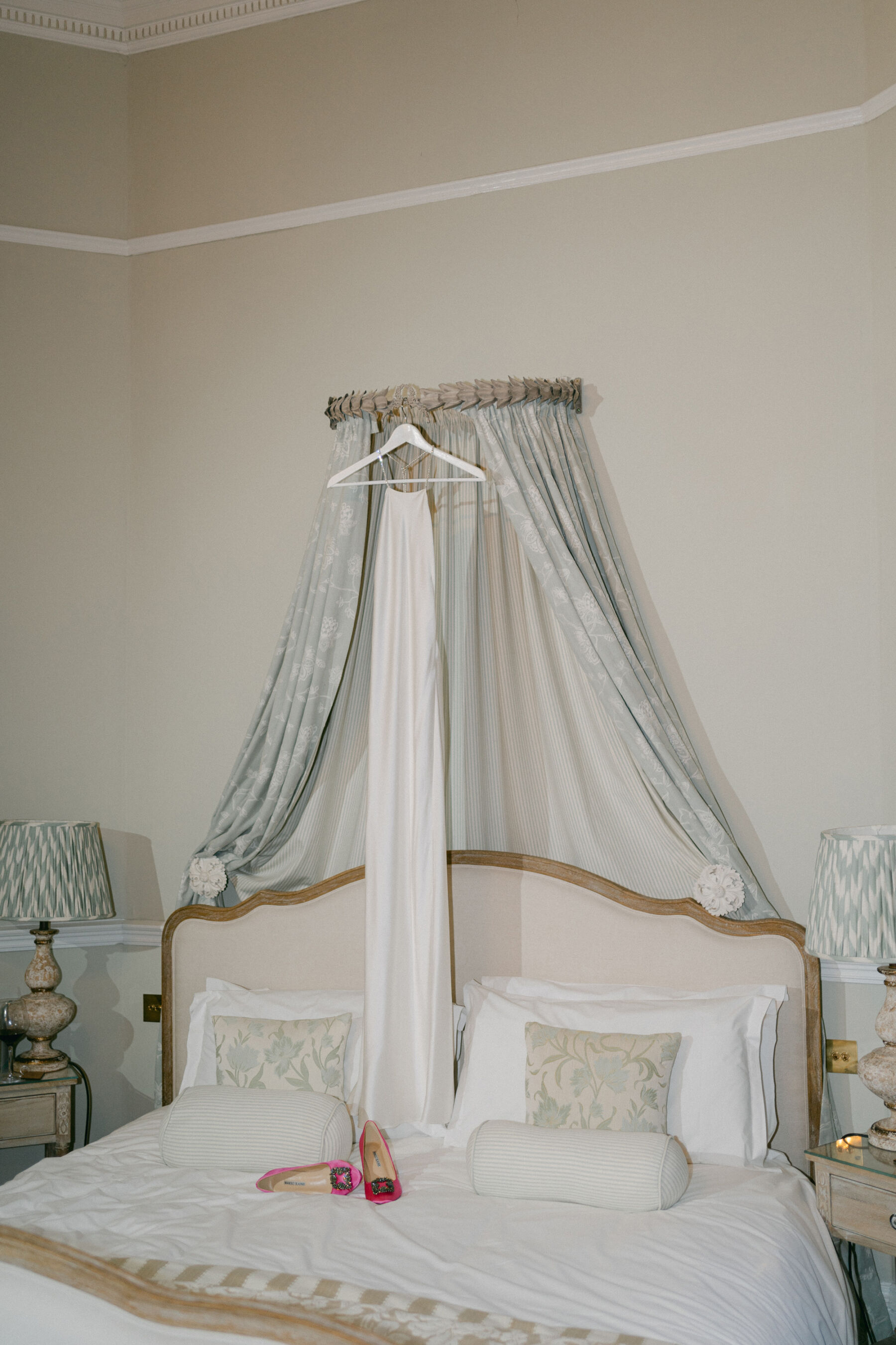 Elegant double bed with a halterneck wedding dress on a hanger and a pair of pink Manolo Blahnik high heel wedding shoes rested on the bed.