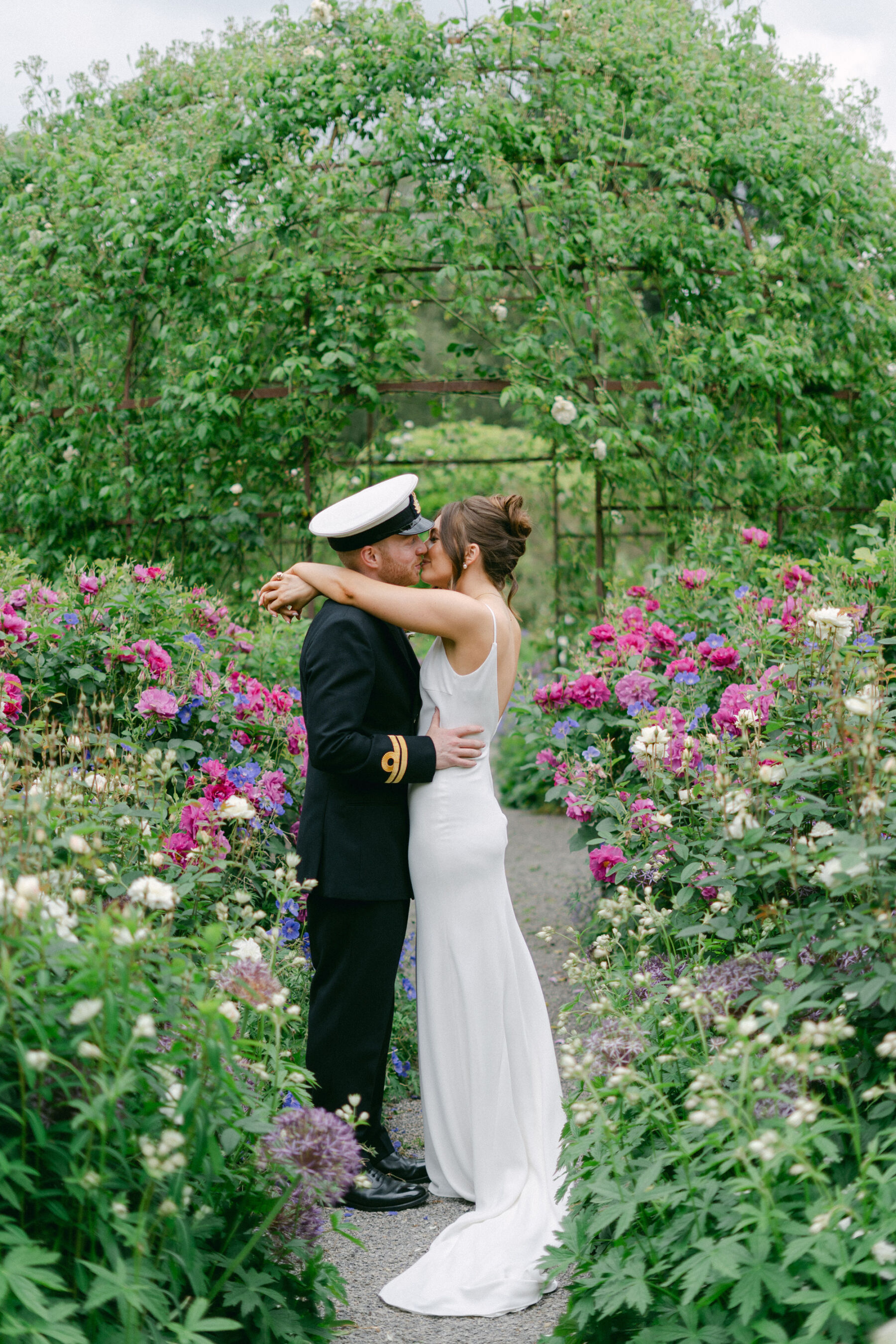 Navy officer in military uniform embracing the bride in the gardens of Middleton Lodge.