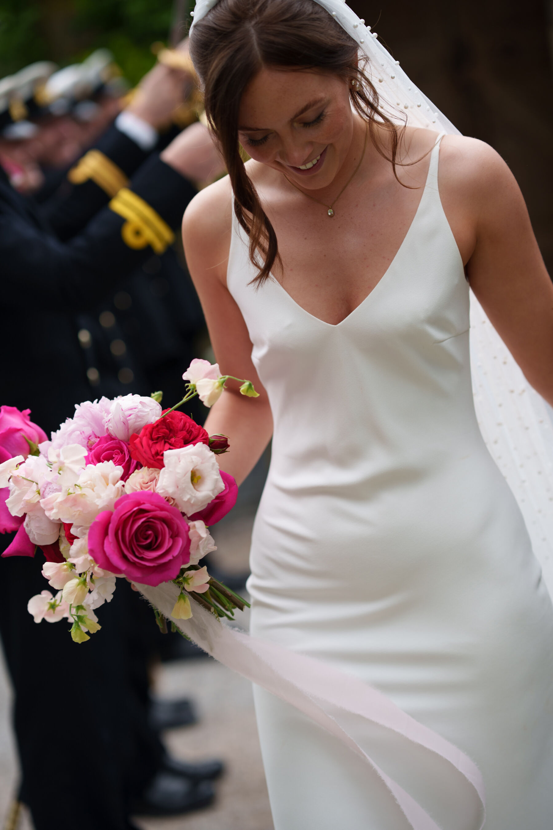The bride wears a minimalist dress and carries a bouquet of sweet peas and roses in various shades of pink with an elegant long pale pink silk ribbon.