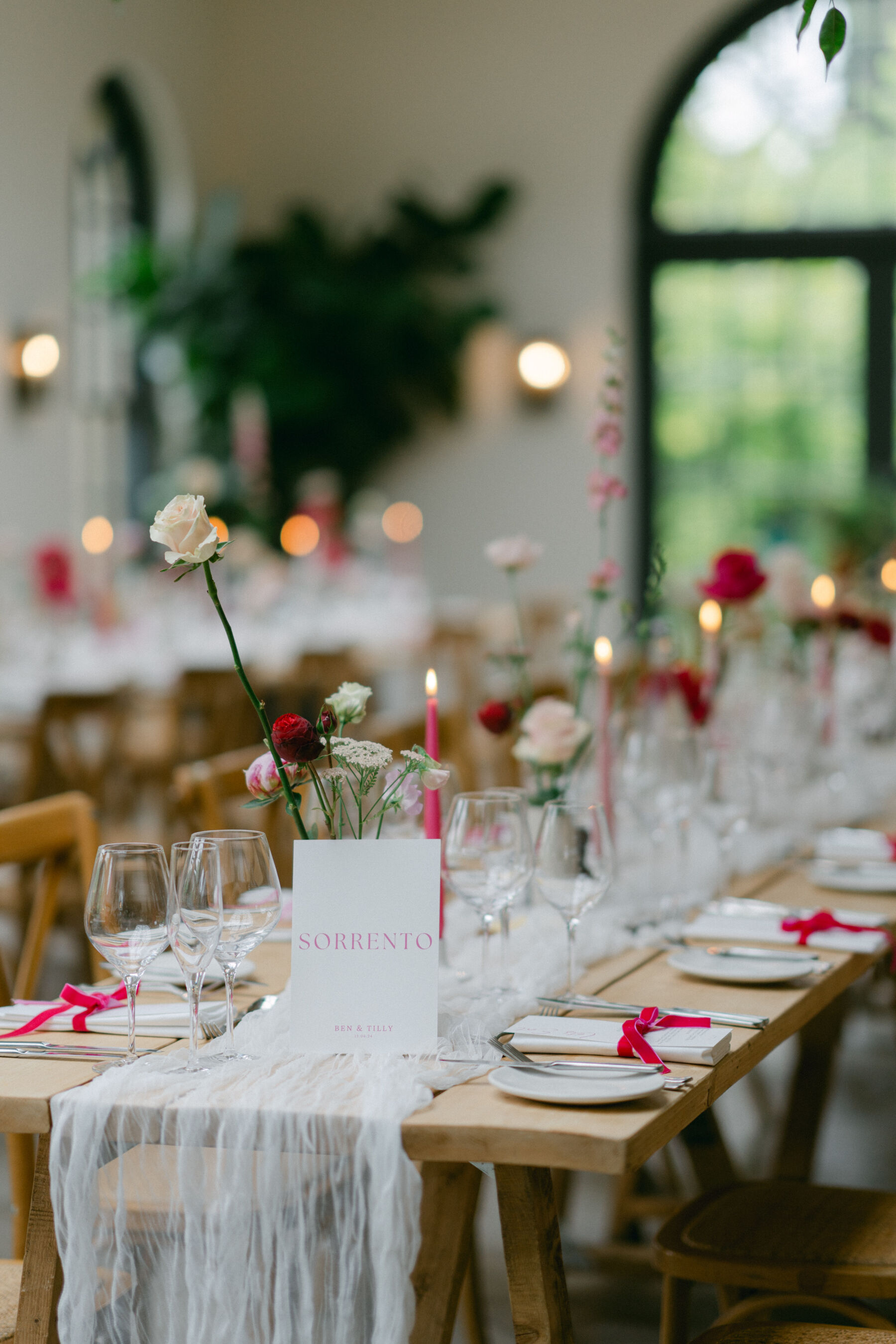 Middleton Lodge wedding decor with place settings including a menu tied with pink velvet ribbon, tall pink taper candles and tall flowers in bud vases. 