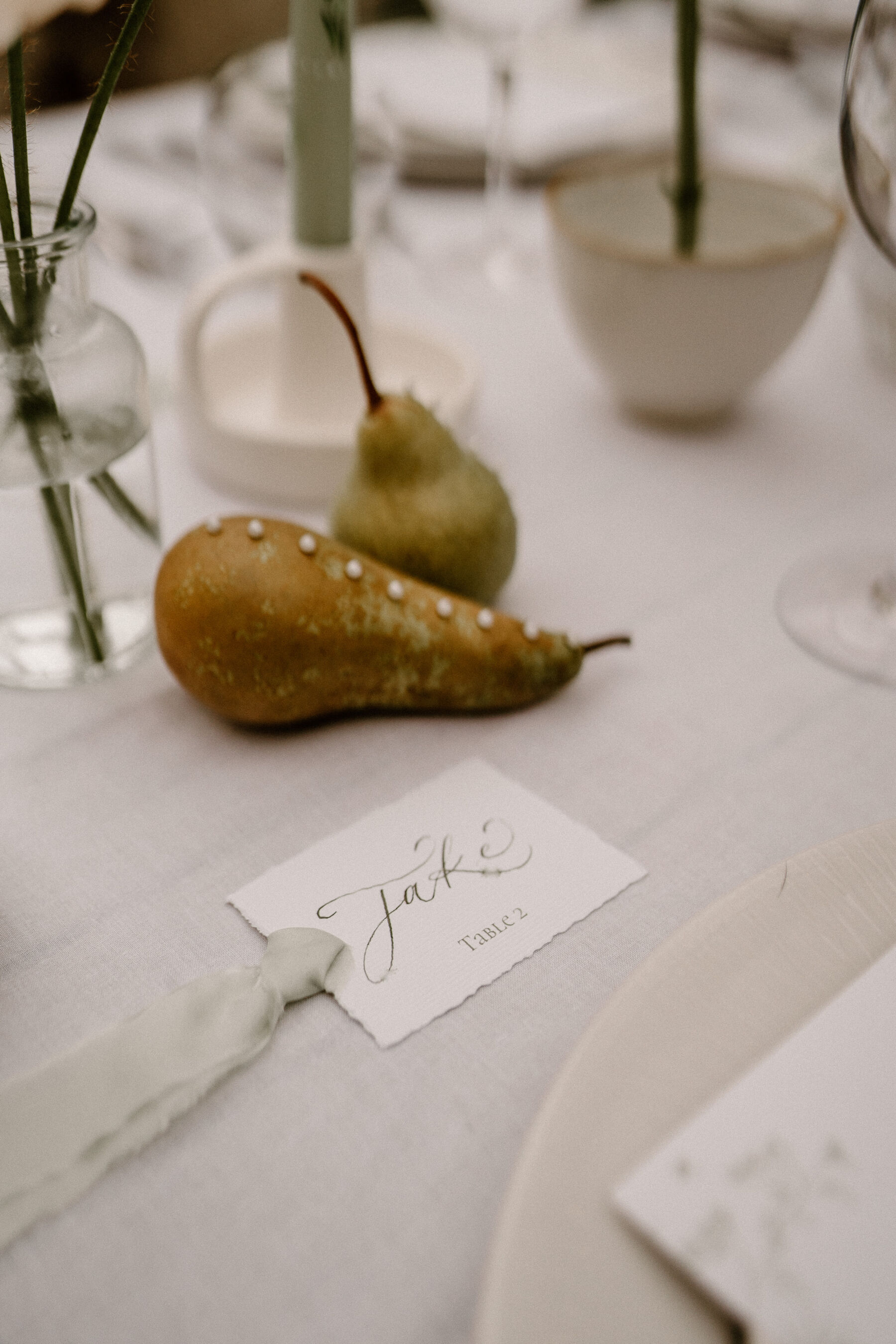 Pear with pearls - modern contemporary wedding table decor. Nearby is a calligraphy tag with a sage green silk ribbon.