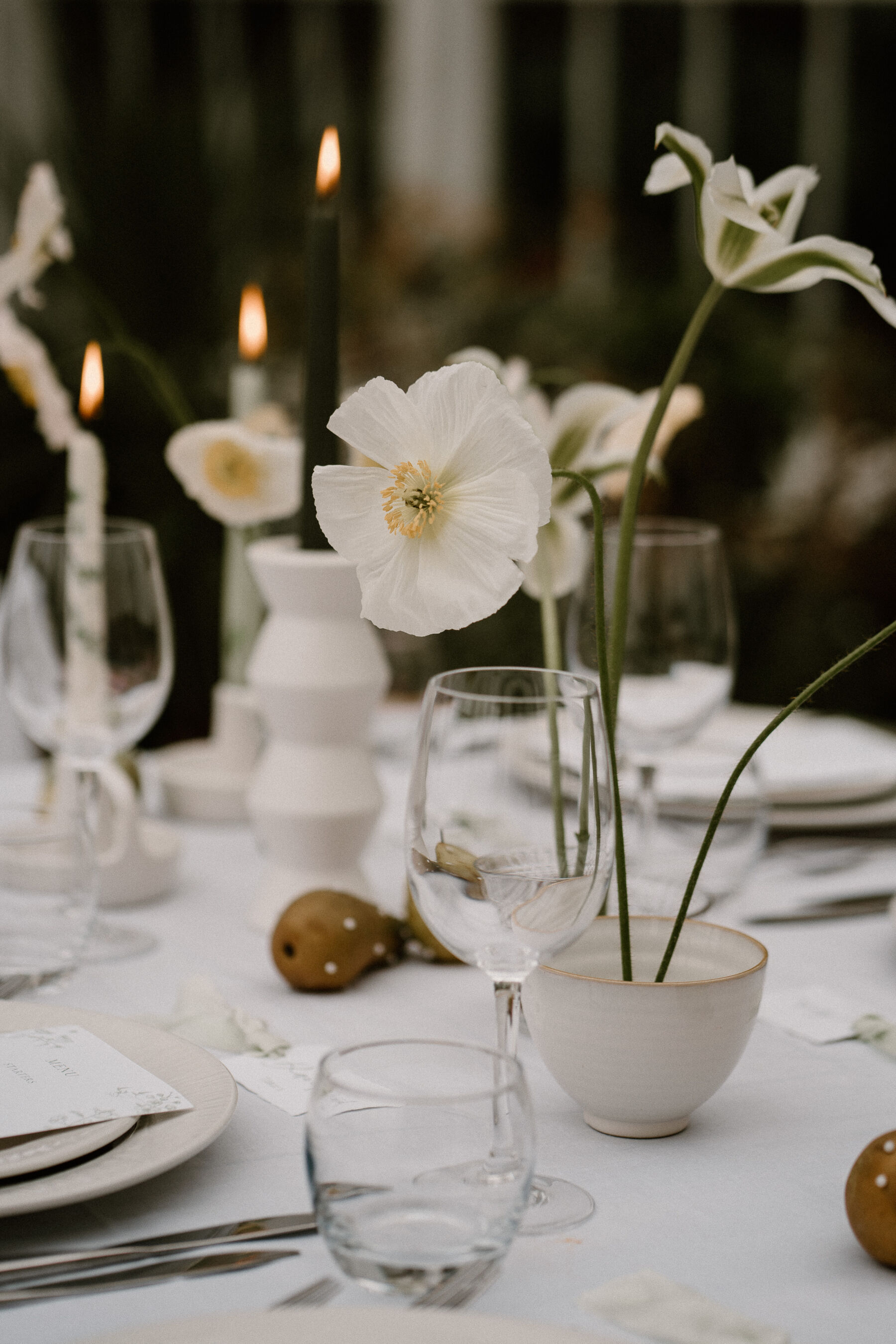 Minimalist spring wedding flowers in ceramic bowls using a floral frog. Taper candles in the background. Elegant spring wedding table decor.