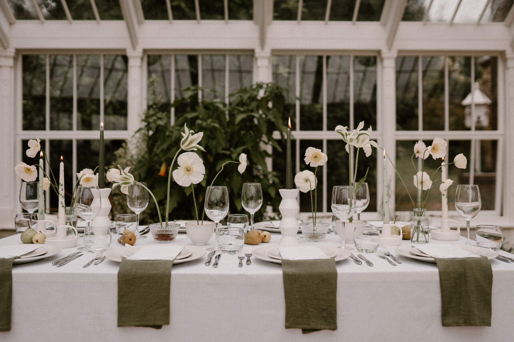 Elegant spring wedding table setting with sage green napkins, minimalist spring flowers in small bowls and dark green and hand painted tapered candles.