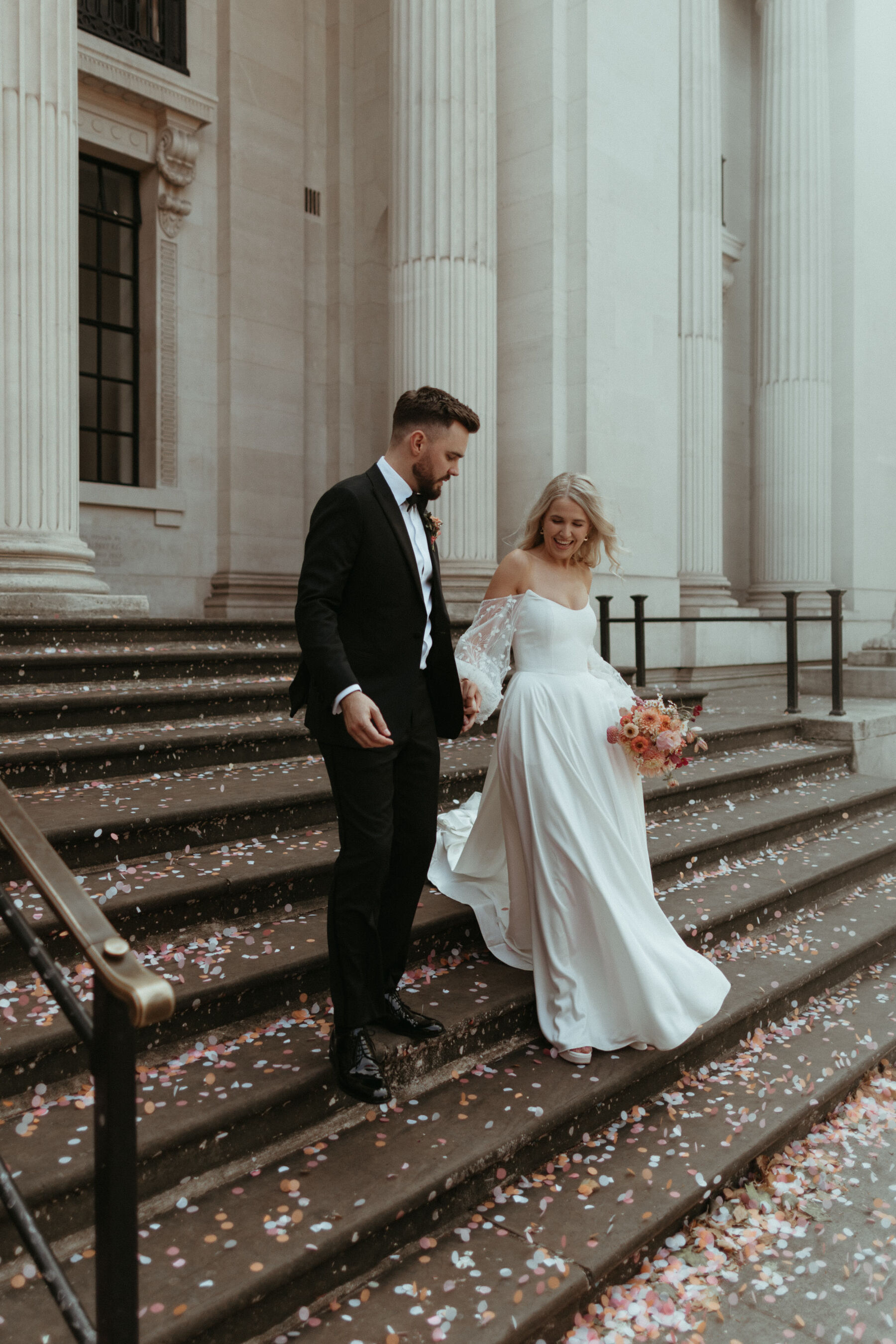 Georgia in Truvelle for her Modern London Wedding at The Depot in Islington 13 Couple walking down the steps that are covered in pastel colour confetti, at Old Marylebone Town Hall in London.