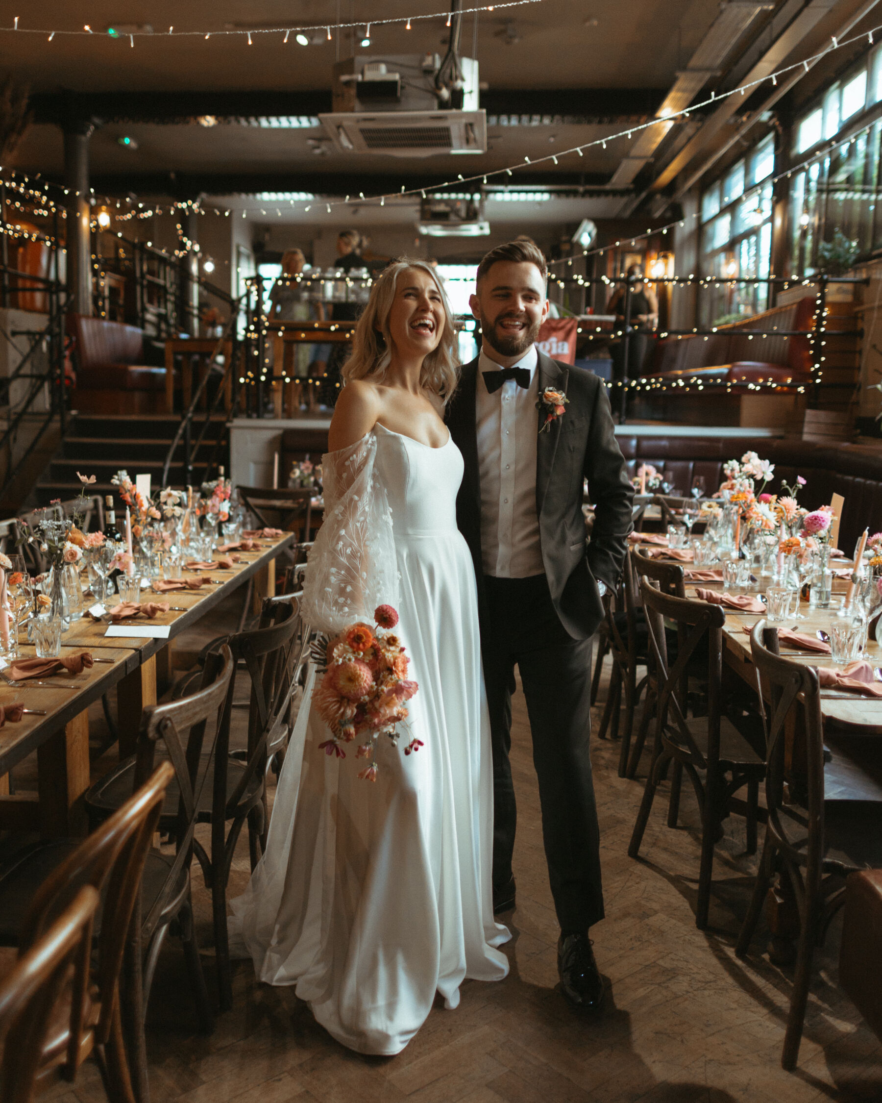 Georgia in Truvelle for her Modern London Wedding at The Depot in Islington 26 Bride and groom standing between their decorated wedding tables at The Depot pub in London.