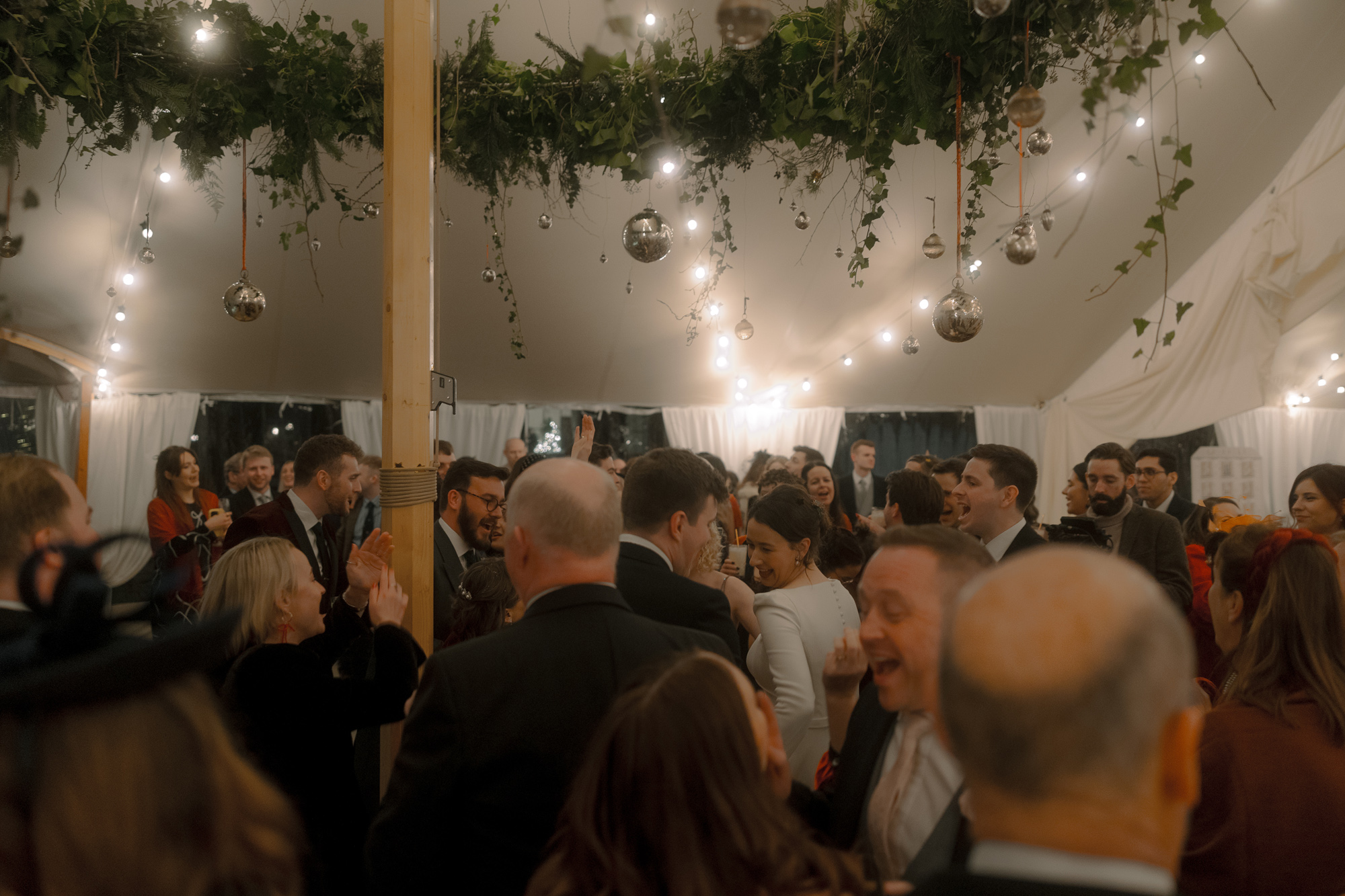 A Movie & Literary Inspired Romantic Christmas Wedding 93 Christmas wedding marquee with greenery hanging from above and festoon lights.