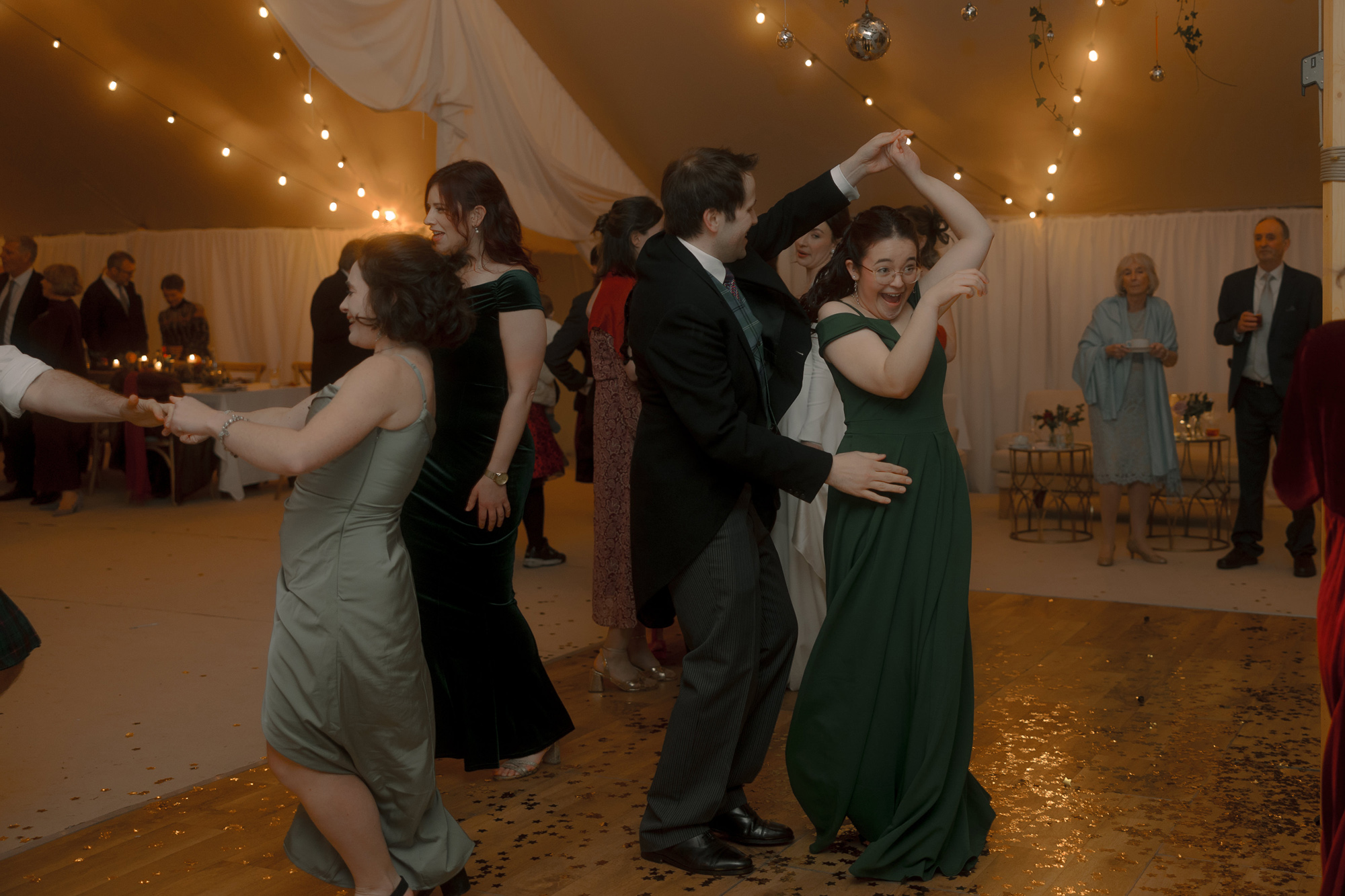 A Movie & Literary Inspired Romantic Christmas Wedding 94 Wedding guests dancing on a wedding marquee dance floor at a Christmas wedding, surrounded by festoon lights.