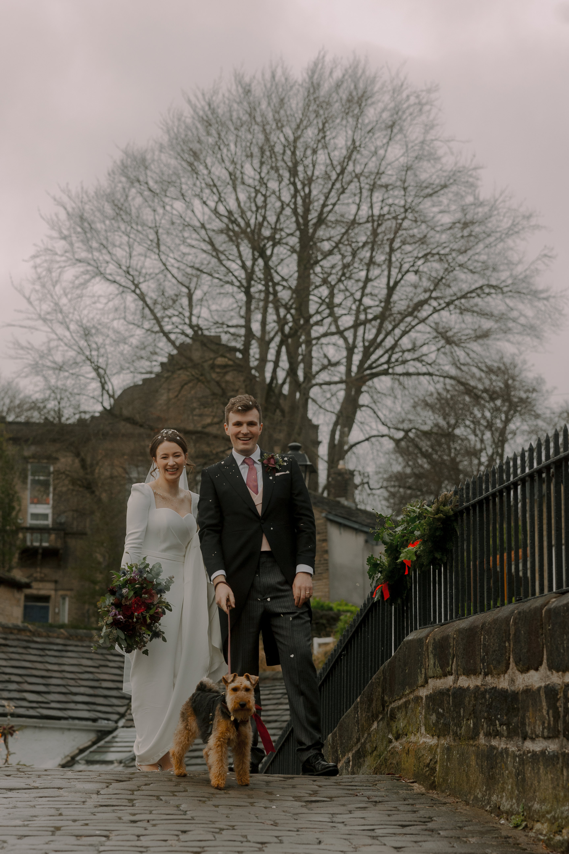 A Movie & Literary Inspired Romantic Christmas Wedding 54 Bride and groom on their Christmas wedding day. The bride wears Suzanne Neville and carries a winter wedding bouquet with. red roses. They are accompanied by their dog.