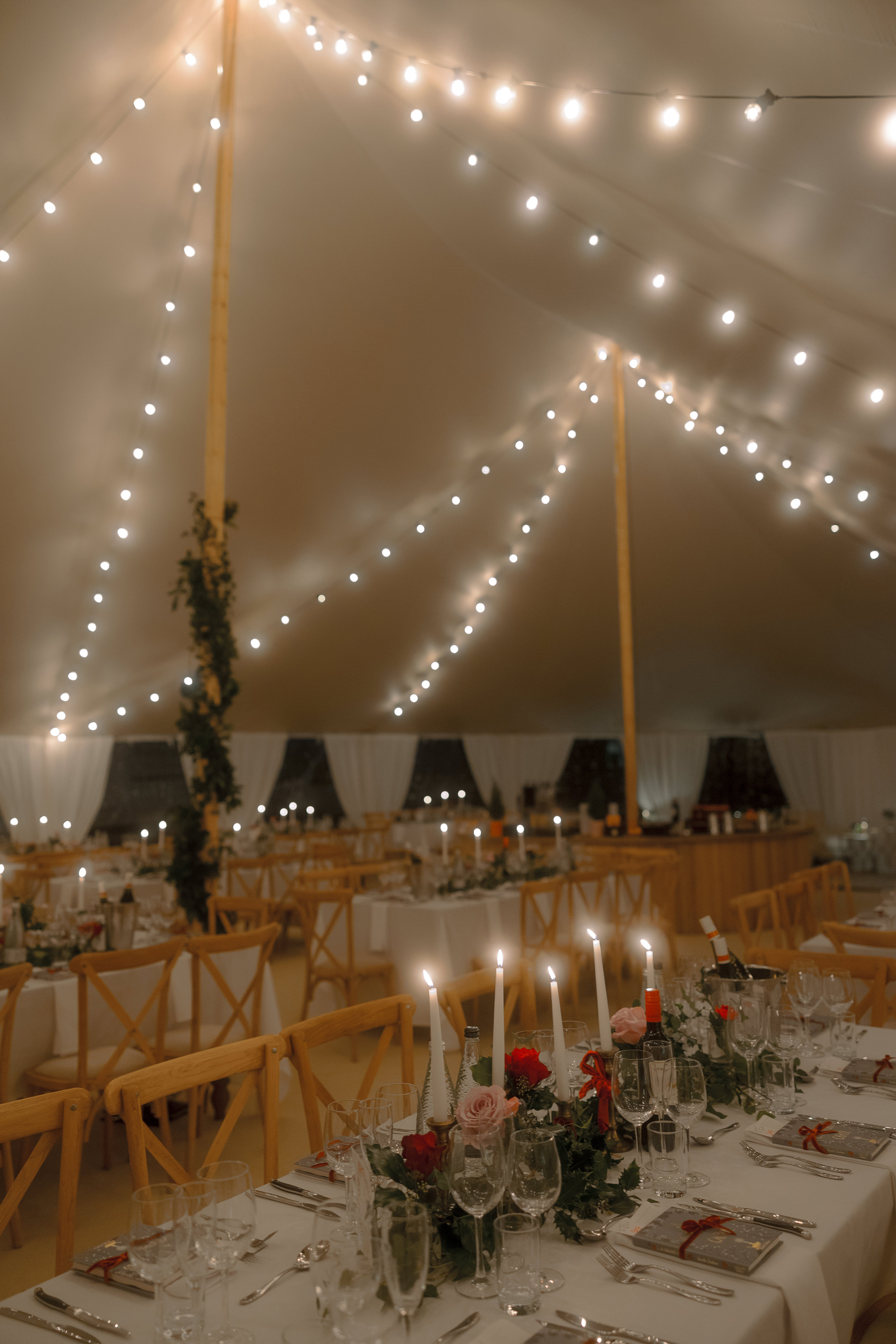 A Movie & Literary Inspired Romantic Christmas Wedding 66 Candlelit Christmas wedding marquee with festoon lights. Tables decorated with pink and red roses and taper candles.