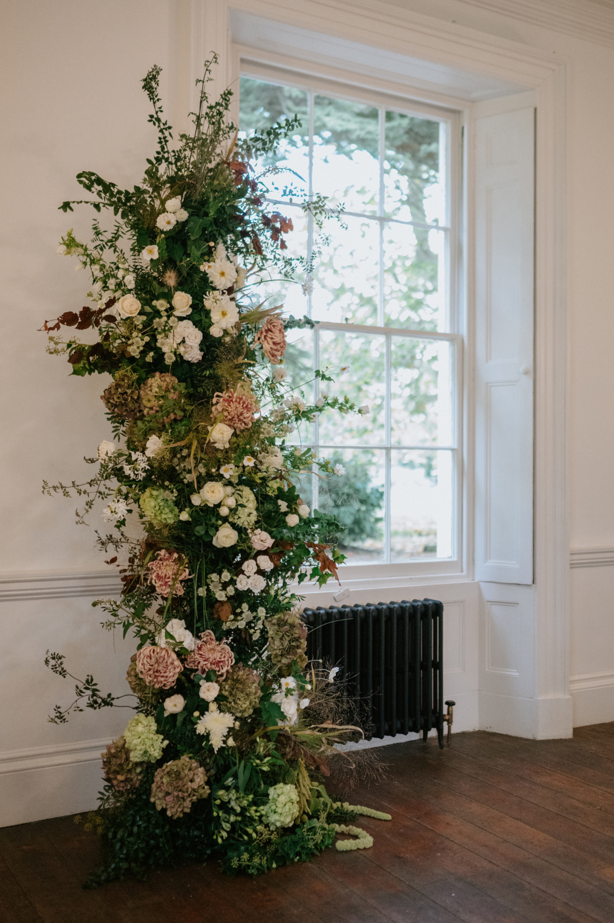 Phoebe in Jesus Peiro for her Elegant November Wedding at Aswarby Rectory 35 Indoor broken floral arch with hydrangea and dahlia - standing by a window at Aswarby Rectory wedding venue.