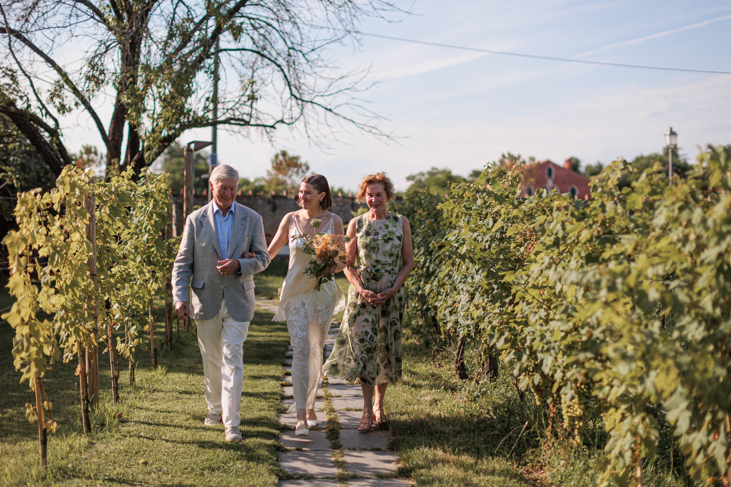 Danielle Frankel Intimate Italian Wedding 45 - Kathryn in Danielle Frankel for her Intimate Italian Wedding Bride walking to her outdoor wedding ceremony with her mother and father.