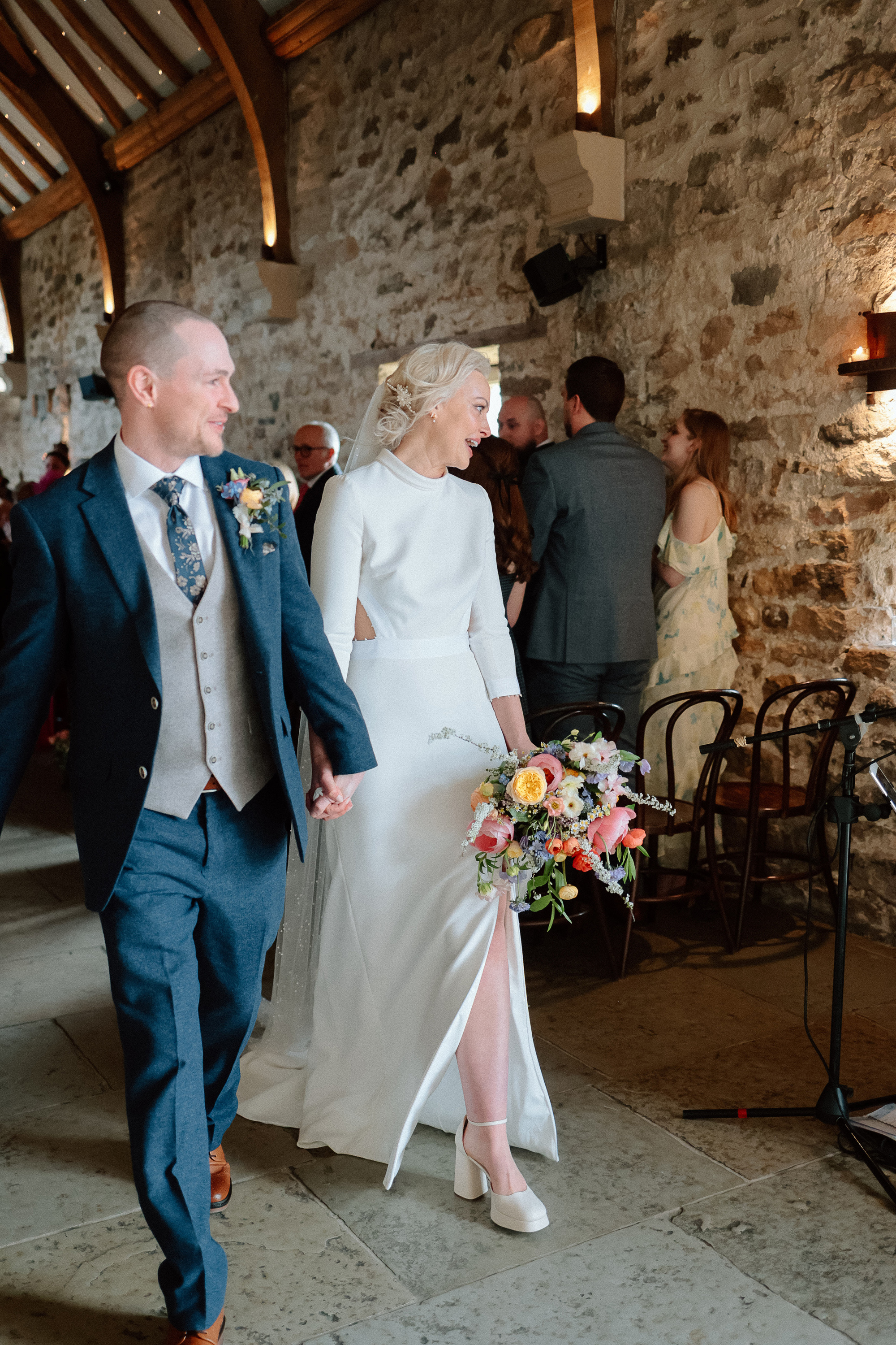 Bon Bride Elegance for a Stylish Healey Barn Wedding in Northumberland 24 Bride and groom holding hands and walking down a aisle. She wears Bon Bride and carries a colourful wedding bouquet.