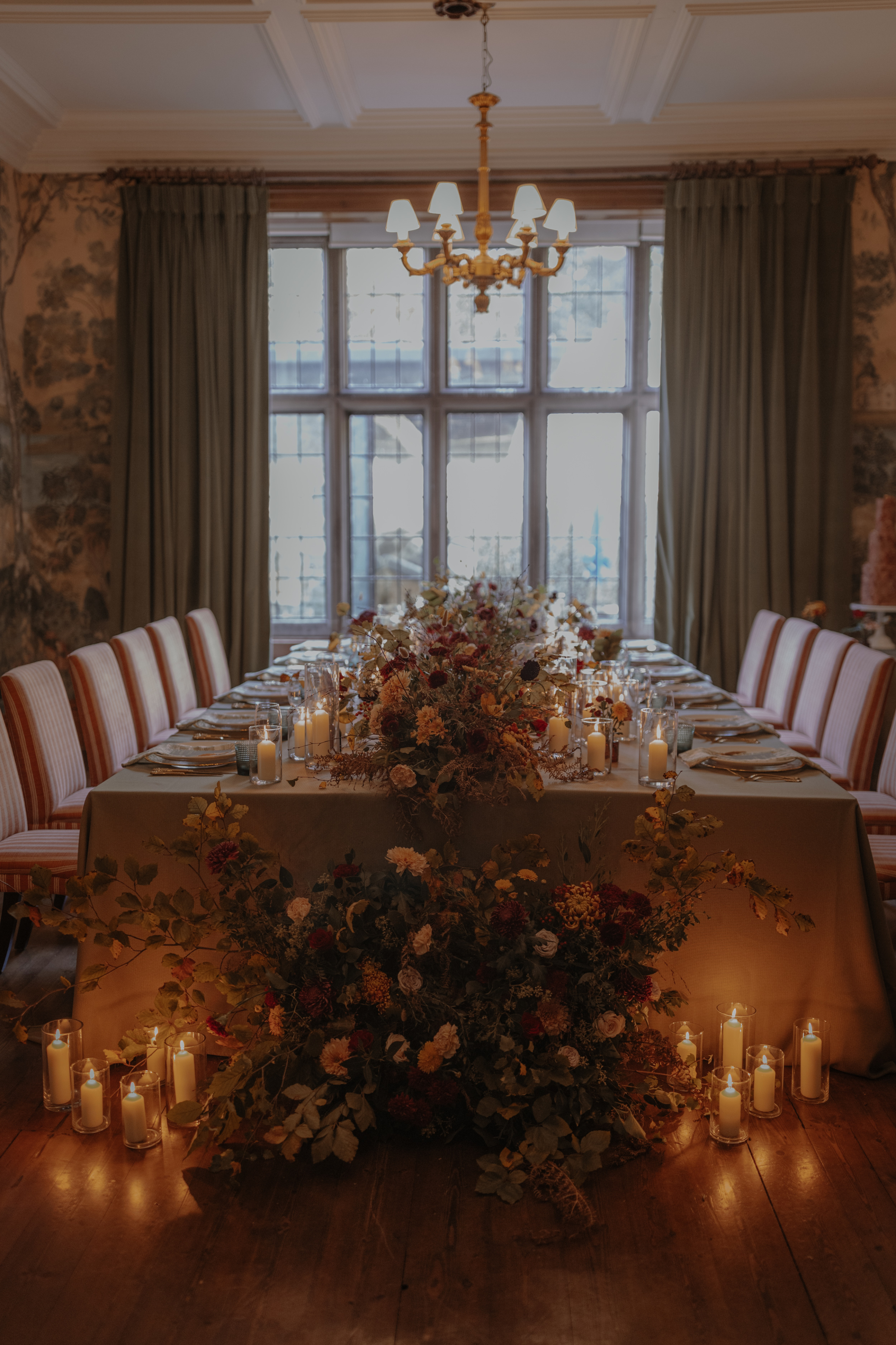 Elegant wedding table setting with the appearance of flowers tumbling off the edge of the table onto the floor, surrounded by candles in hurricane jars.