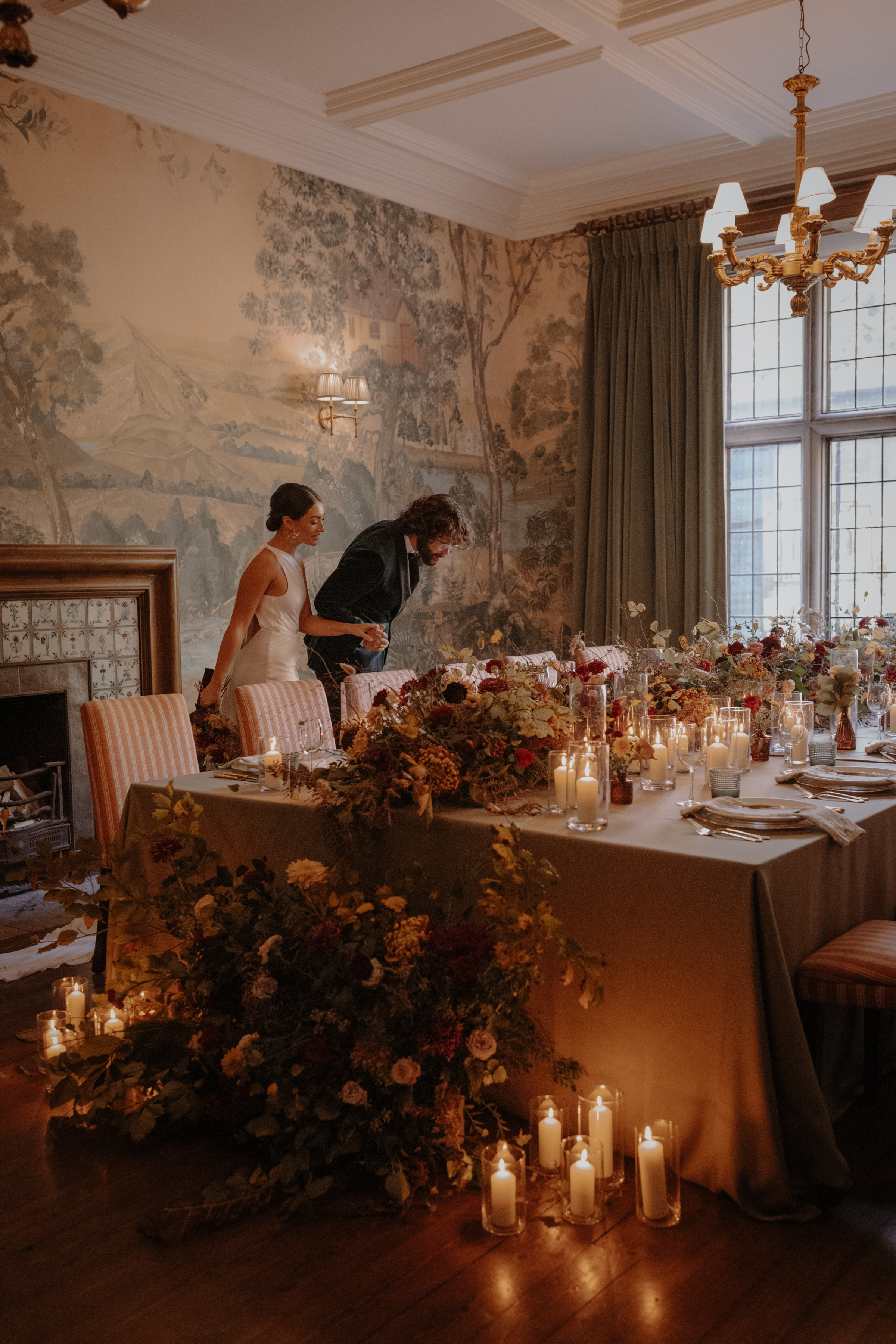 A Little Wild, A Little Luxe: Helen Rose Photography's Beautiful Peak District Editorial 27 Bride and groom leaning over to examine the detail at their wedding reception table that is decorated with an abundance of Autumn wedding flowers and candles.